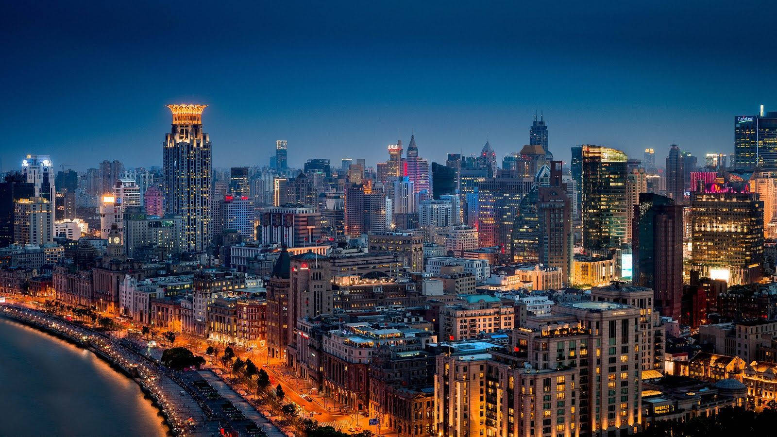 Chengdu 桌布 壁紙 — 一個令人眼花繚亂的夜景城市景觀，沿著海濱有燈火通明的摩天大樓和發光的街道，在深藍色的天空下。