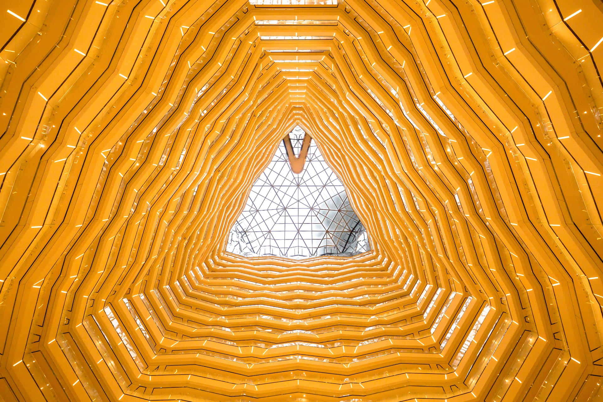 Yellow Pattern 桌布 壁紙 — 一個令人著迷的向上視角，穿過金色波浪形隧道，露出上方幾何玻璃天花板。