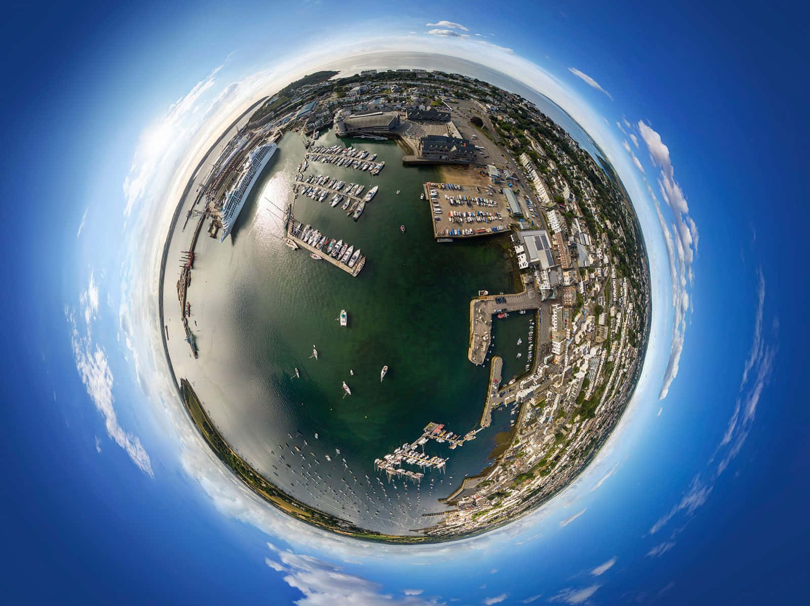 海洋 桌布 壁紙 — 一個令人驚嘆的360度魚眼視角，俯瞰海岸港口，船隻停泊，建築物環繞水面，天空湛藍明亮。