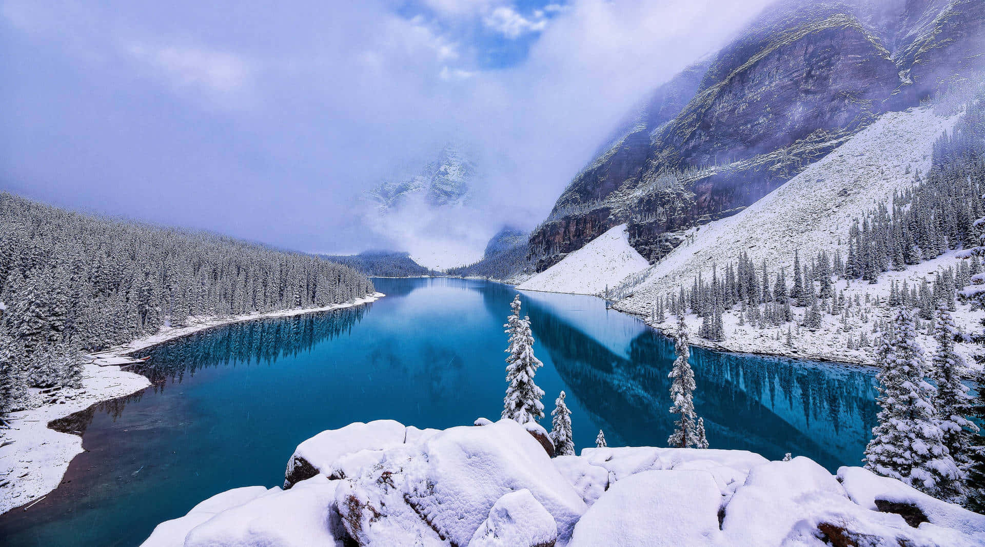Cozy Winter Desktop 桌布 壁紙 — 一個令人驚嘆的冬季景色，一個充滿活力的綠松石湖坐落在白雪覆蓋的山脈和常綠森林之間，天空多雲。