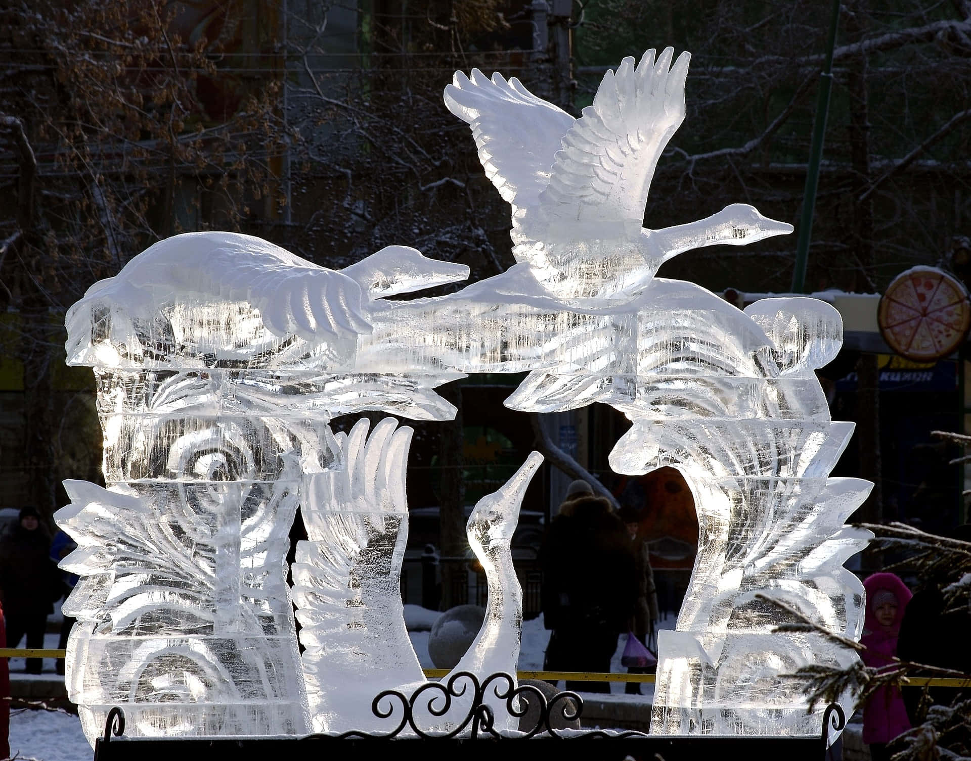 Ice Sculpture 桌布 壁紙 — 一個令人驚嘆的冰雕，描繪飛翔和站立的天鵝，羽毛細節精緻，背景是雪景城市。