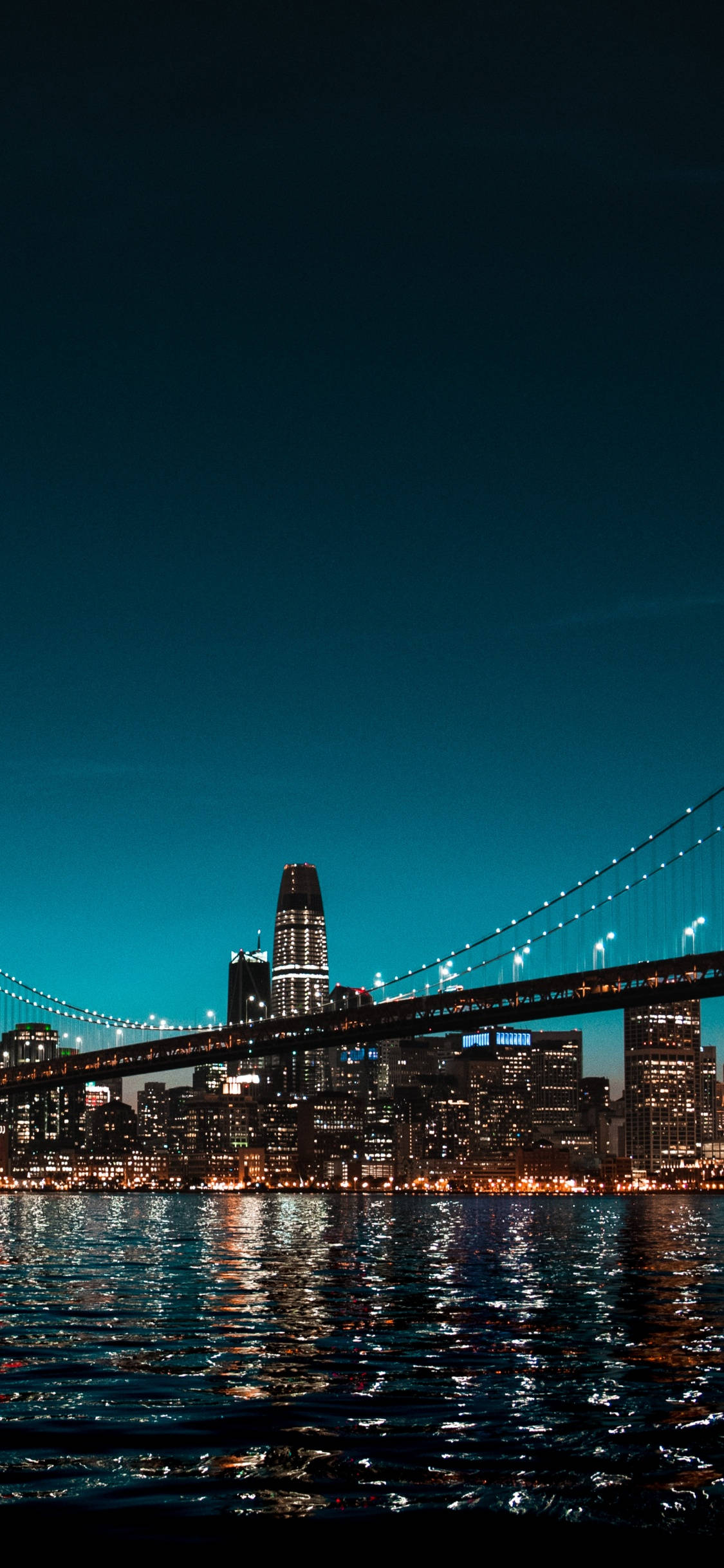 Brooklyn Bridge 桌布 壁紙 — 一個令人驚嘆的夜景城市景觀， featuring 一座亮燈的吊橋橫跨水面，摩天大樓在深藍綠色天空下閃耀。