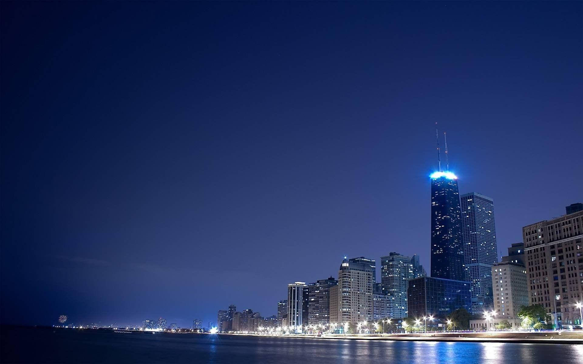 quiet 桌布 壁紙 — 一個令人驚嘆的夜景城市景觀，有一座高聳的摩天大樓在深靛藍色的天空中發出藍色光芒，其燈光倒映在下方平靜的水面上。