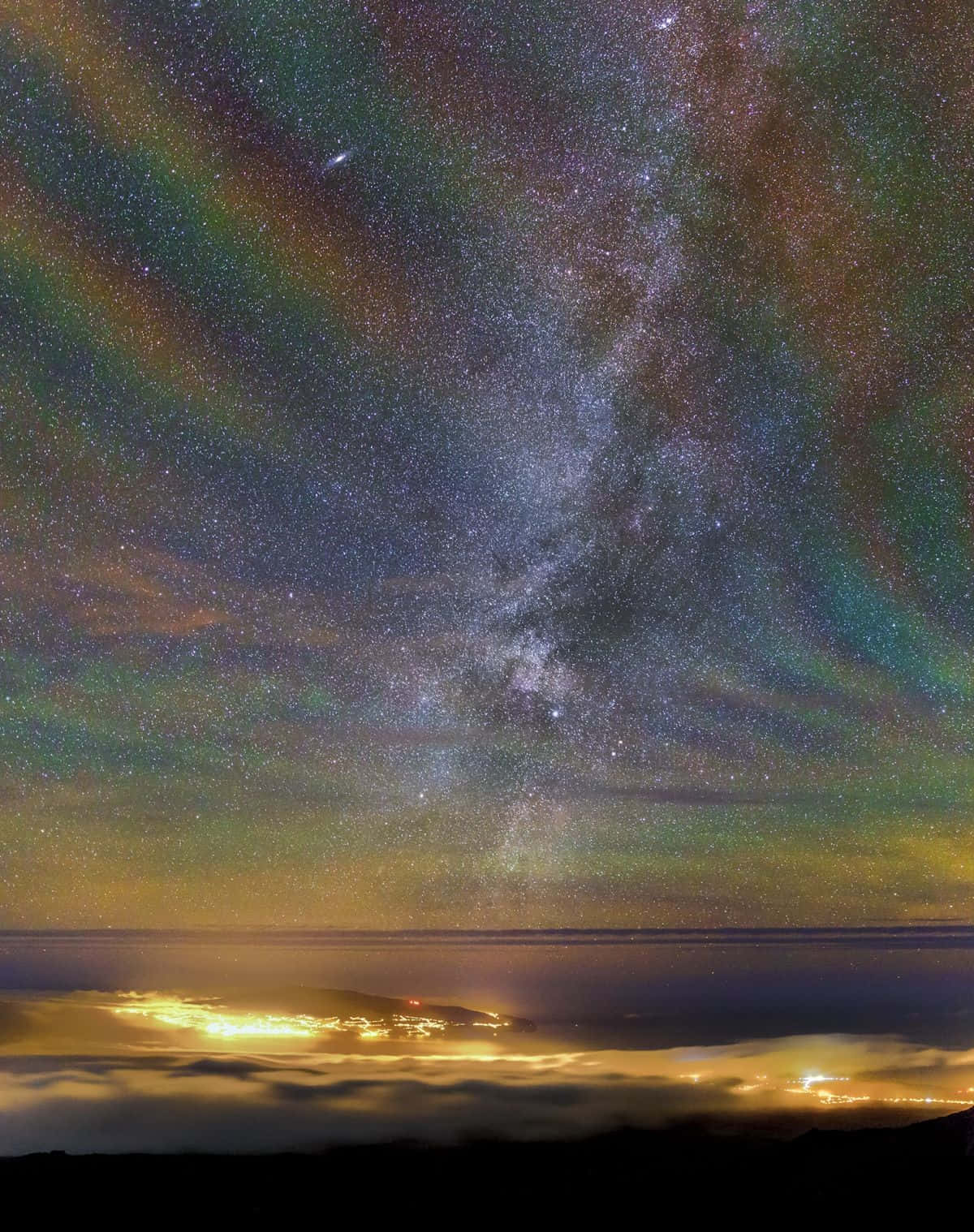 Galaxy Rainbow 桌布 壁紙 — 一個令人驚嘆的夜空，充滿星星和色彩繽紛的極光，拱形在發光的雲海之上，下方是遙遠的城市燈光。