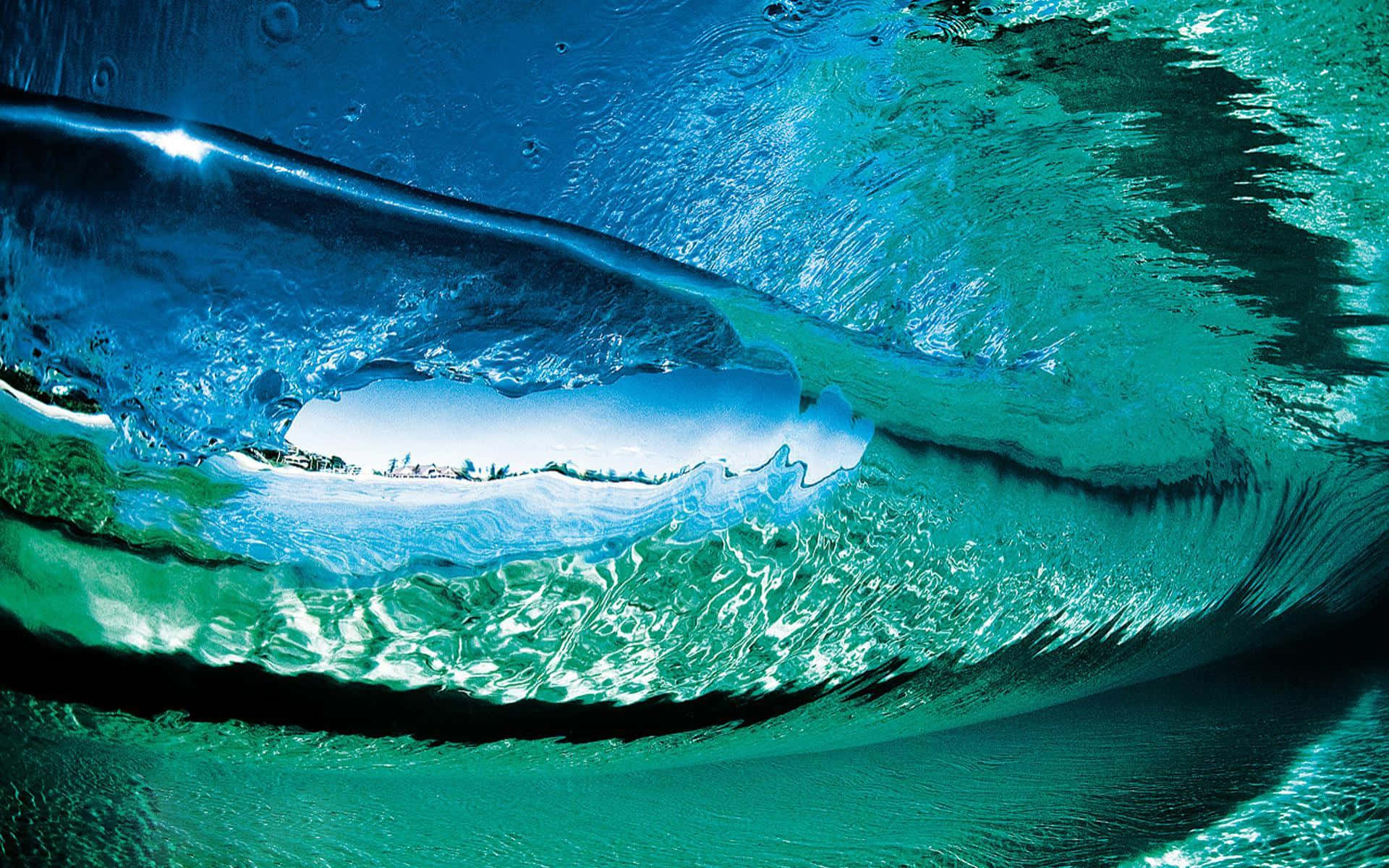 Ocean Waves 桌布 壁紙 — 一個令人驚嘆的水底視角，展示一道捲曲的海浪，透過其半透明的藍綠色弧線，顯露出明亮的天空和遙遠的海岸線。
