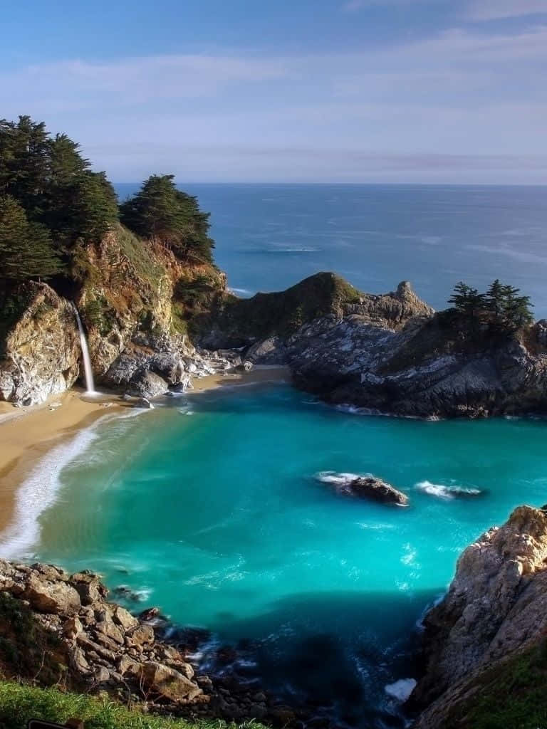 自然風景動圖 桌布 壁紙 — 一個令人驚嘆的海岸小海灣，擁有碧綠的海水、沙灘和從岩石懸崖傾瀉入海的瀑布。