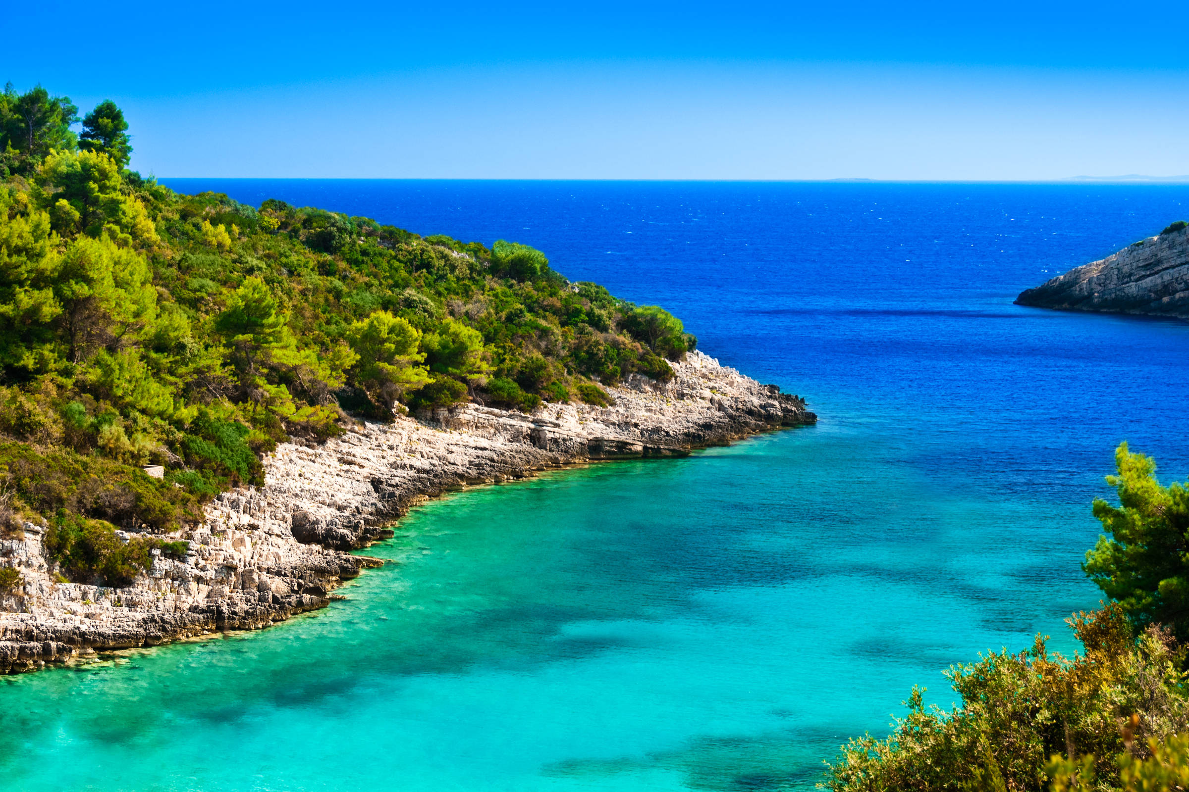 Croatia 桌布 壁紙 — 一個令人驚嘆的海岸小灣，碧綠的海水 nestled 在岩石峭壁之間，峭壁上覆蓋著茂密的綠色植物，在清澈的藍天下。