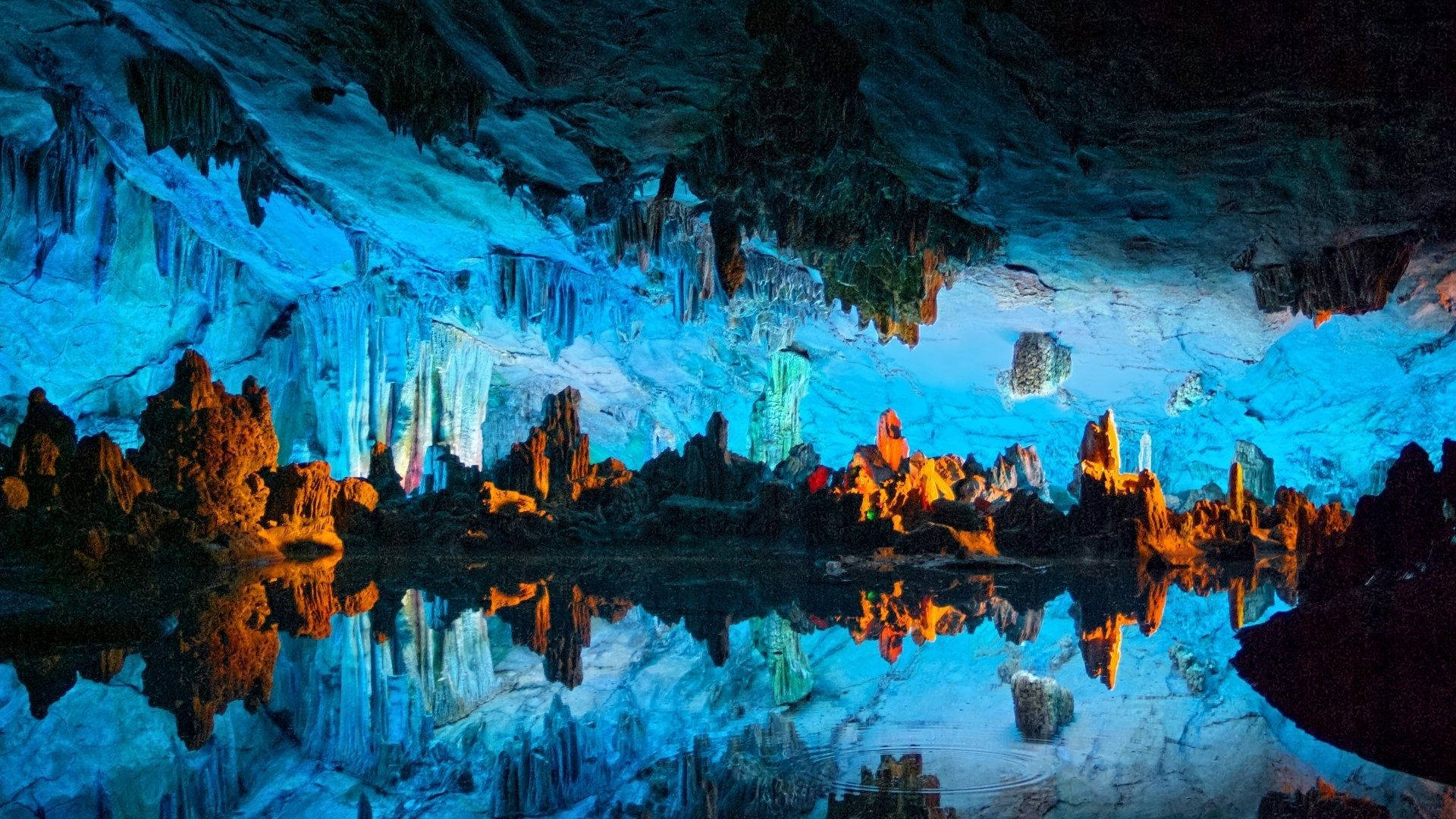 Cave 桌布 壁紙 — 一個令人驚嘆的照明洞穴，藍色和橙色的岩石形態完美地倒映在下方平靜的水面上。