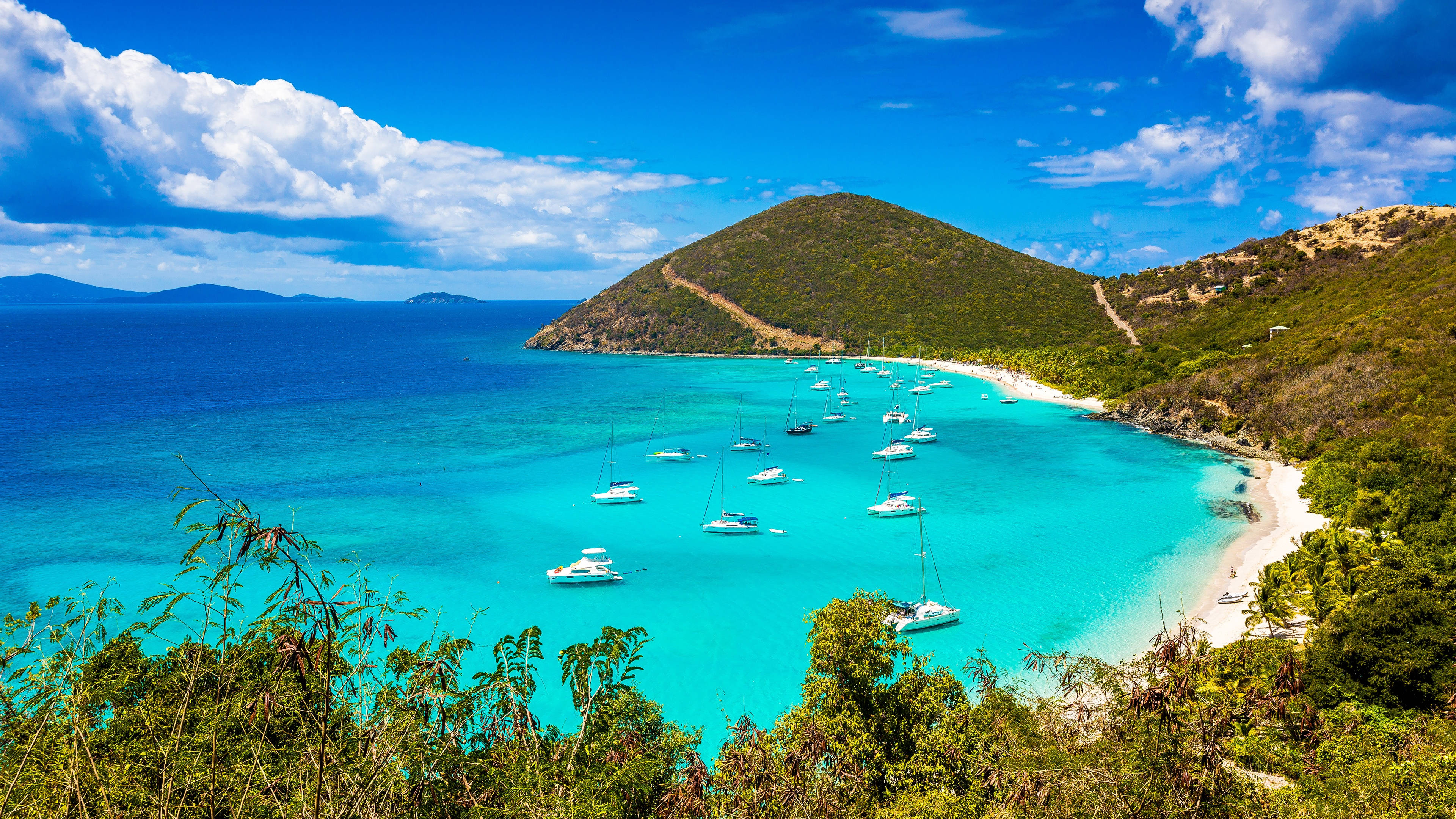Islands 桌布 壁紙 — 一個令人驚嘆的熱帶海灣，碧綠的海水點綴著帆船，坐落在鬱鬱蔥蔥的綠色山丘之間，天空湛藍。