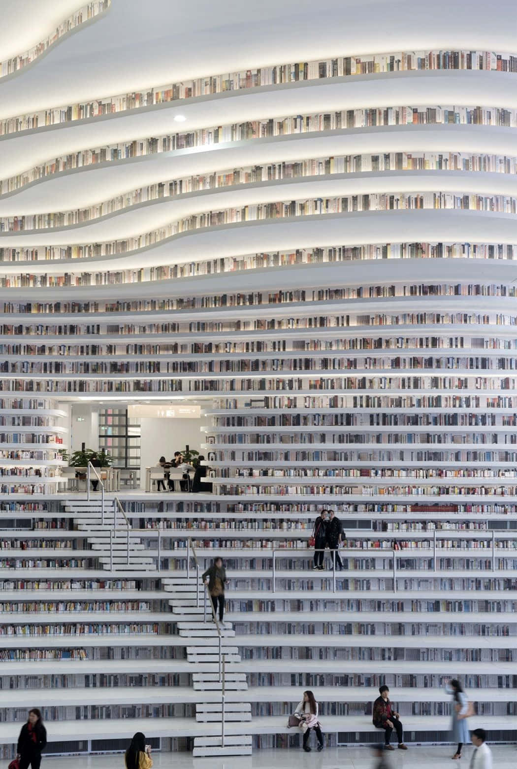 Library 桌布 壁紙 — 一個令人驚嘆的現代圖書館，螺旋形的白色書架上擺滿了書籍，人們在其中走動或坐著。