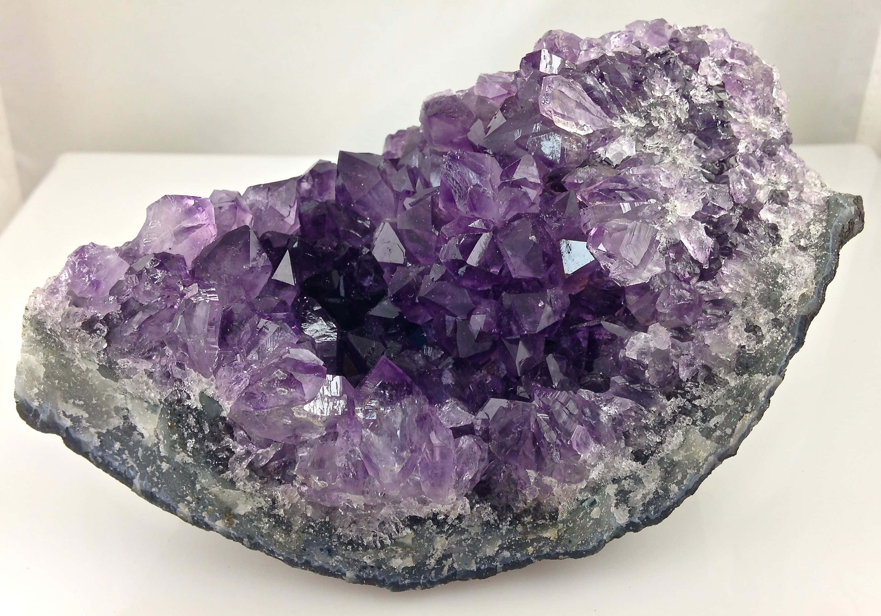 紫水晶 桌布 壁紙 — 一個令人驚嘆的紫水晶晶洞，深紫色晶體在柔和光線下閃耀，背景為潔淨的白色。