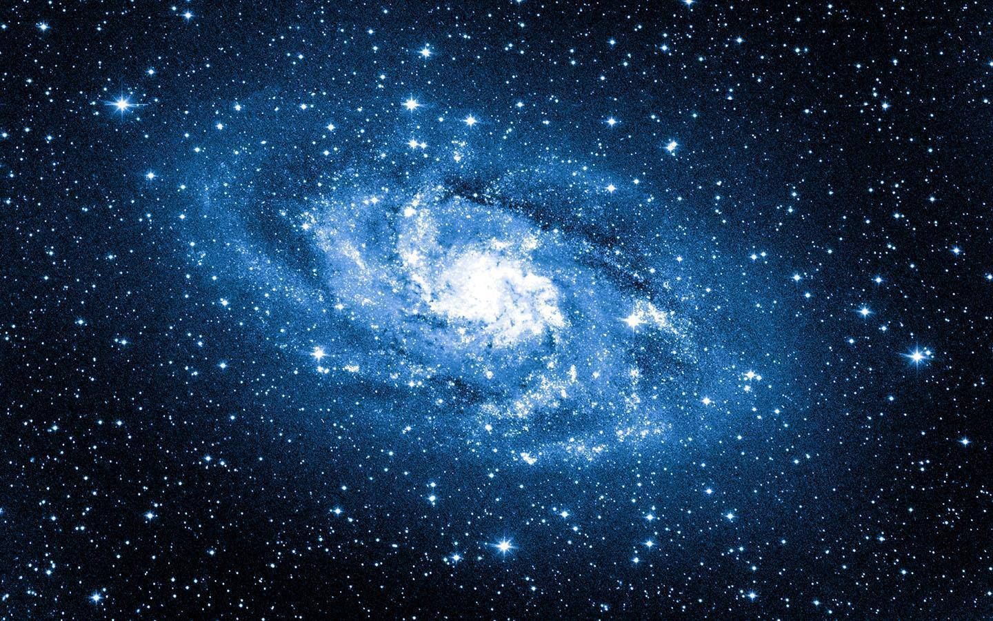 藍色銀河 桌布 壁紙 — 一個令人驚嘆的螺旋星系，在佈滿星星的宇宙背景下發出藍色和白色的光芒。