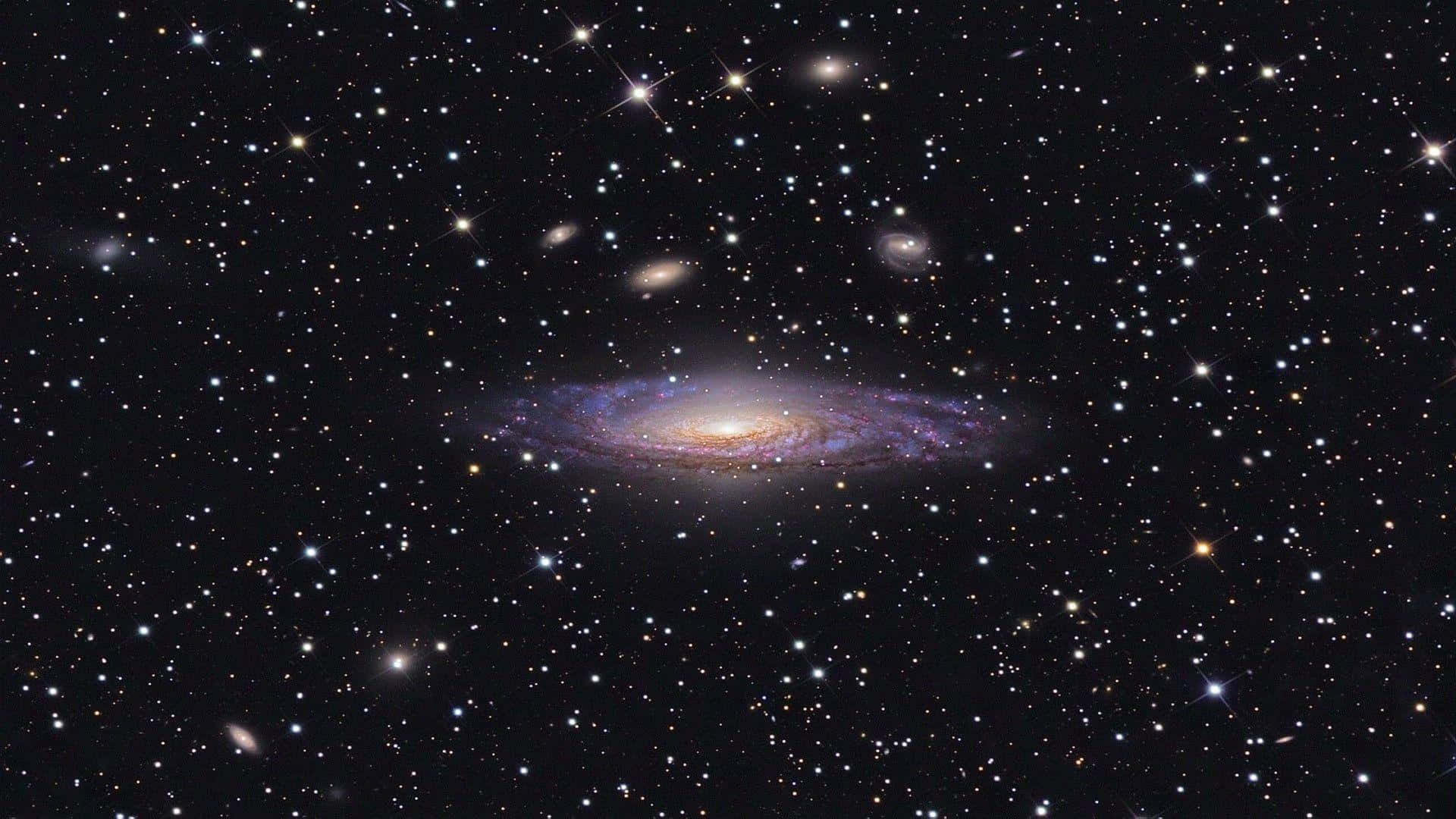 Spiral Galaxy 桌布 壁紙 — 一個令人驚嘆的螺旋星系，帶有發光的紫色和金色旋臂，在深空中無數閃爍星星的背景下閃耀。