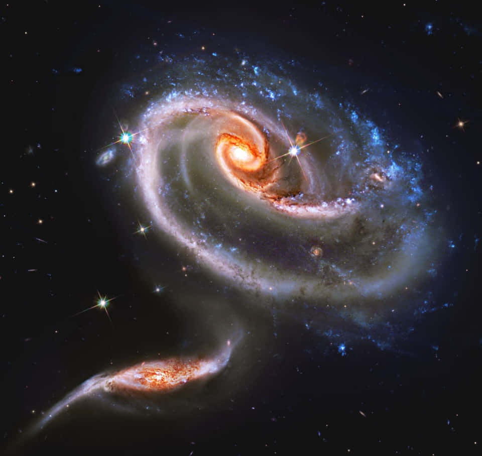 NASA 動態圖片 桌布 壁紙 — 一個令人驚嘆的螺旋星系，帶有發光的橙色核心和藍色星團，在點綴著明亮恆星的黑暗宇宙背景中旋轉。