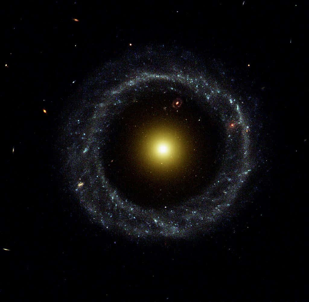 Elliptical Galaxy 桌布 壁紙 — 一個令人驚嘆的螺旋星系，擁有明亮的黃色核心和發光的藍色旋臂，背景是佈滿星空的黑色虛空。
