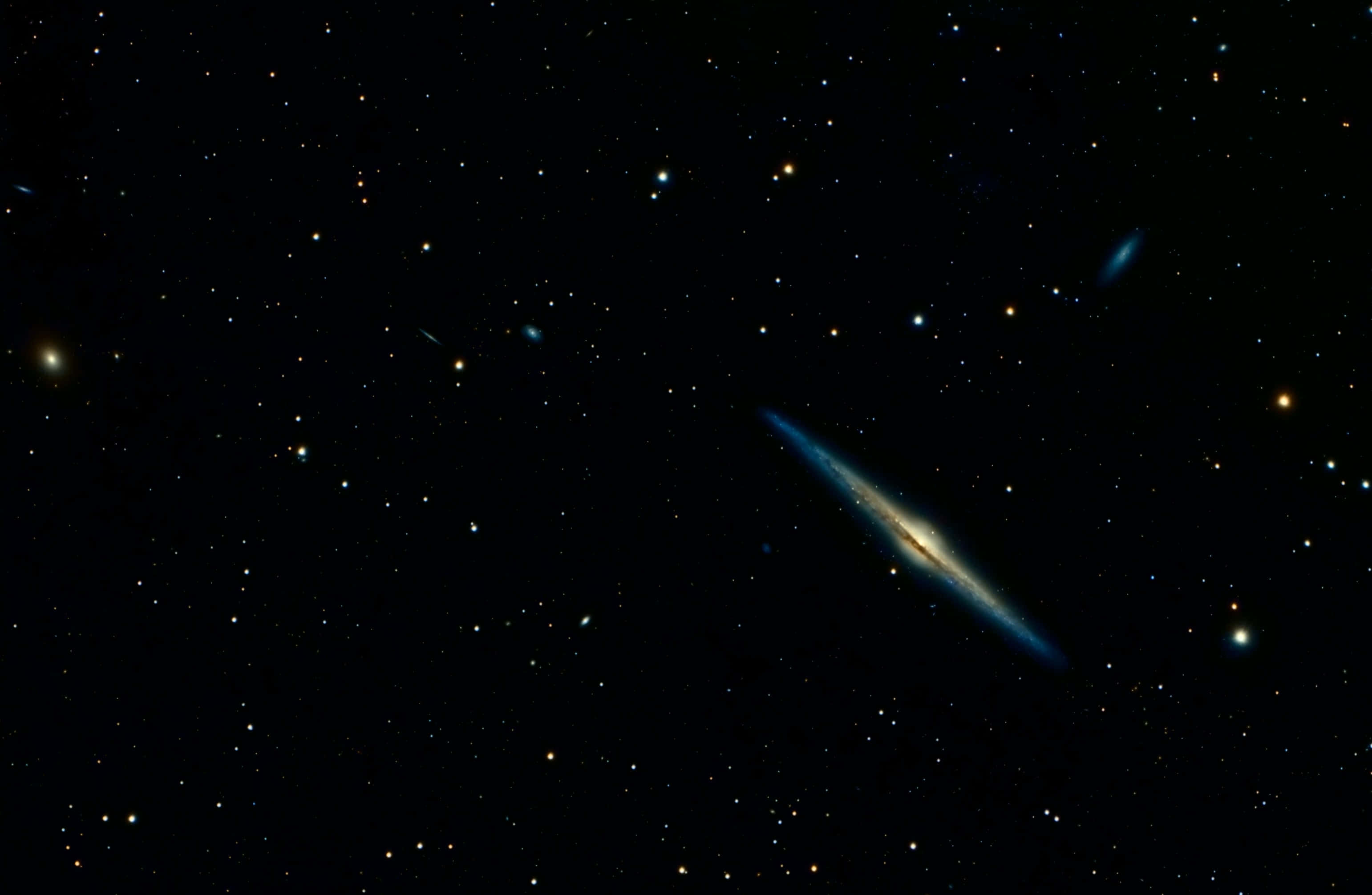 Dark Galaxy 桌布 壁紙 — 一個令人驚嘆的螺旋星系在深空中無數遙遠恆星的背景下發出藍色和黃色的光芒。