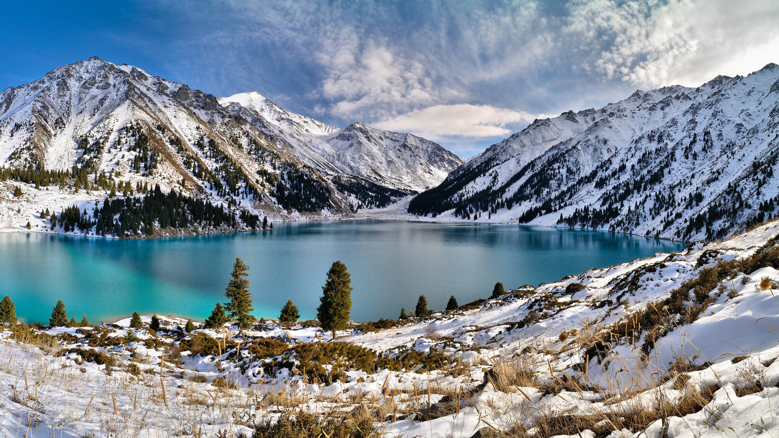 2560x1440 nature 桌布 壁紙 — 一個令人驚嘆的高山湖泊，擁有藍綠色的湖水，坐落在積雪覆蓋的山脈之間，天空部分多雲，呈現藍色。
