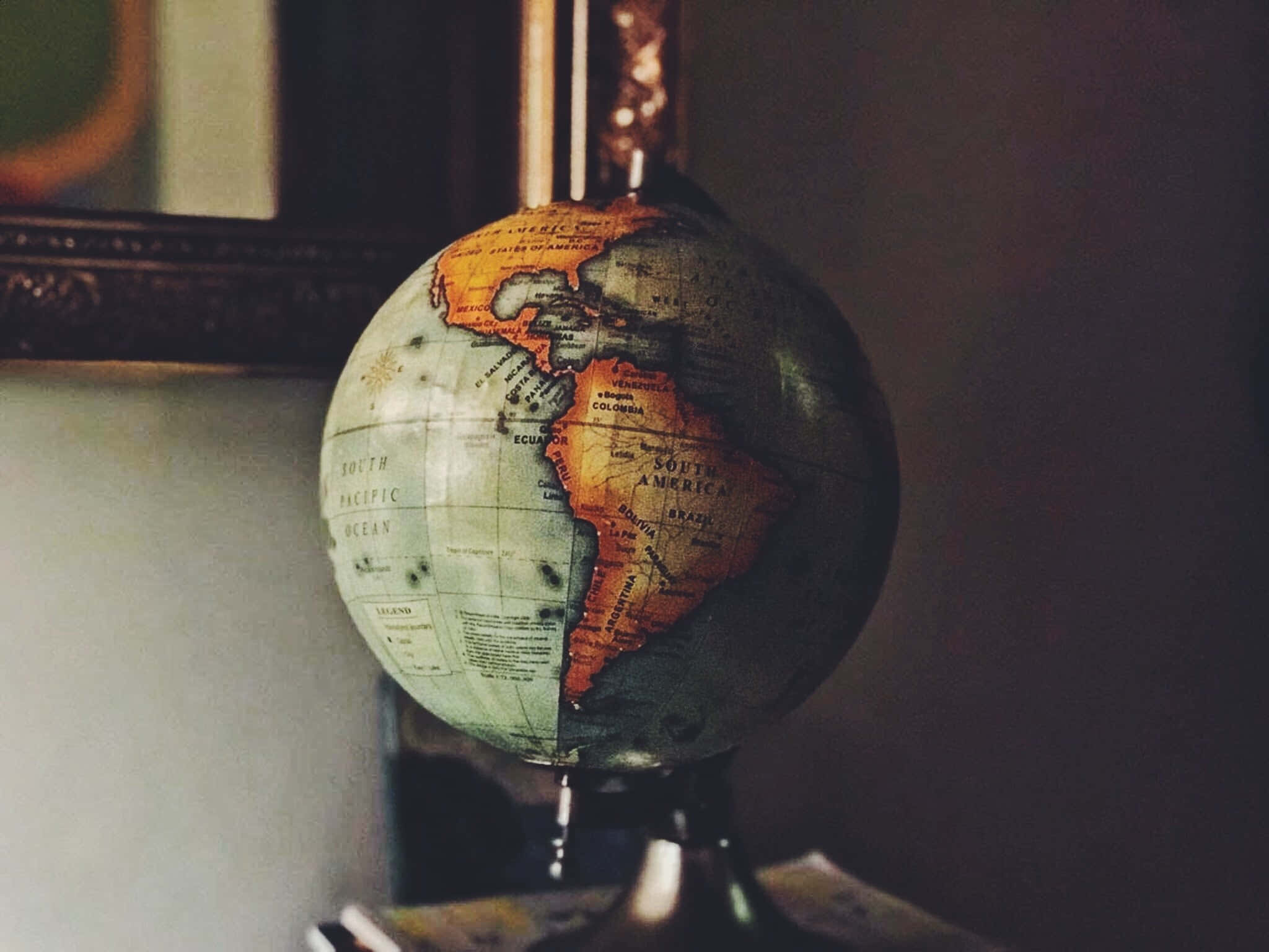 World 桌布 壁紙 — 一個以南美洲為中心的復古地球儀放在支架上，背景有溫暖的燈光和一個帶框的鏡子。