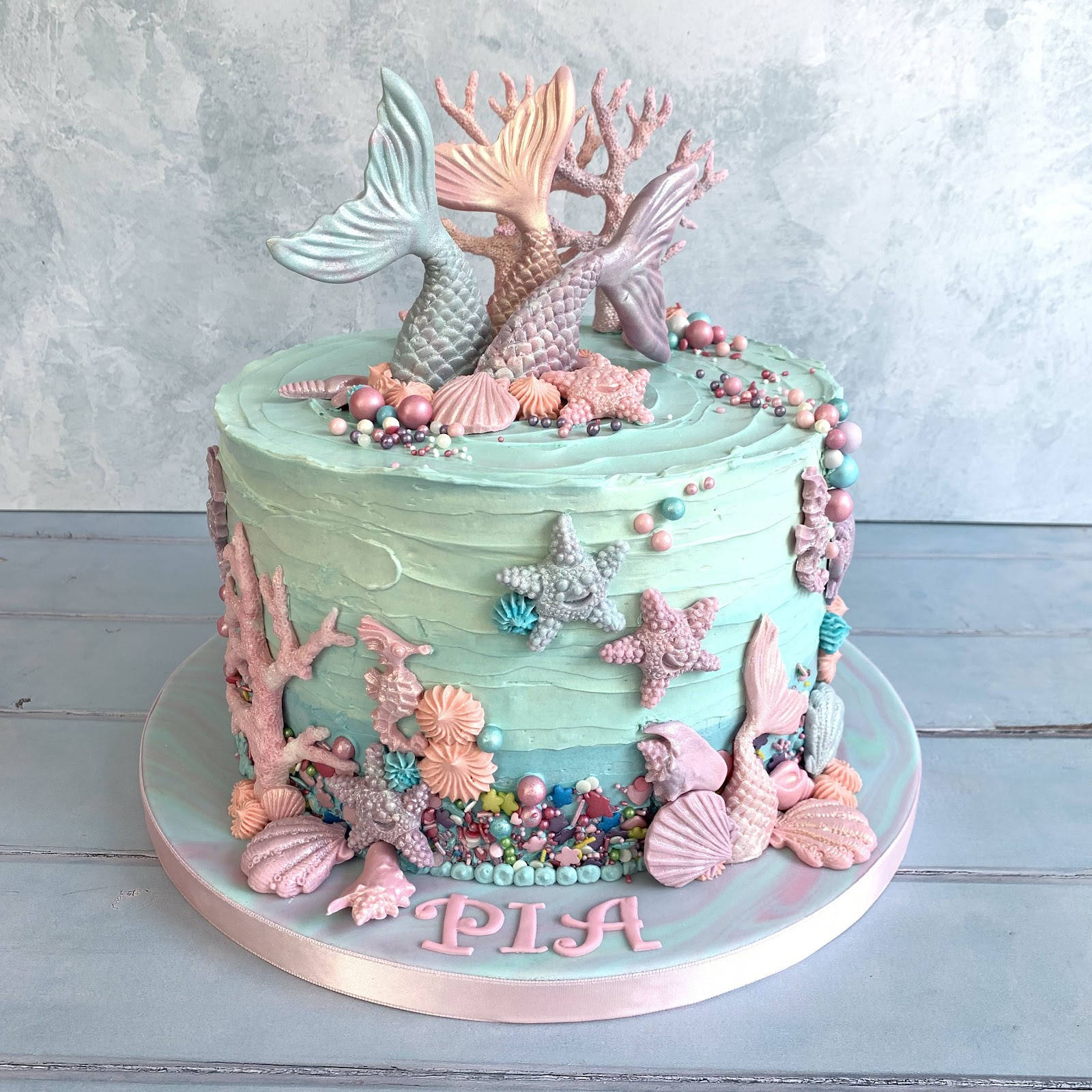 Birthday Cake 桌布 壁紙 — 一個以木質表面裝飾的粉彩美人魚主題蛋糕，綴有糖珊瑚、貝殼和尾巴。