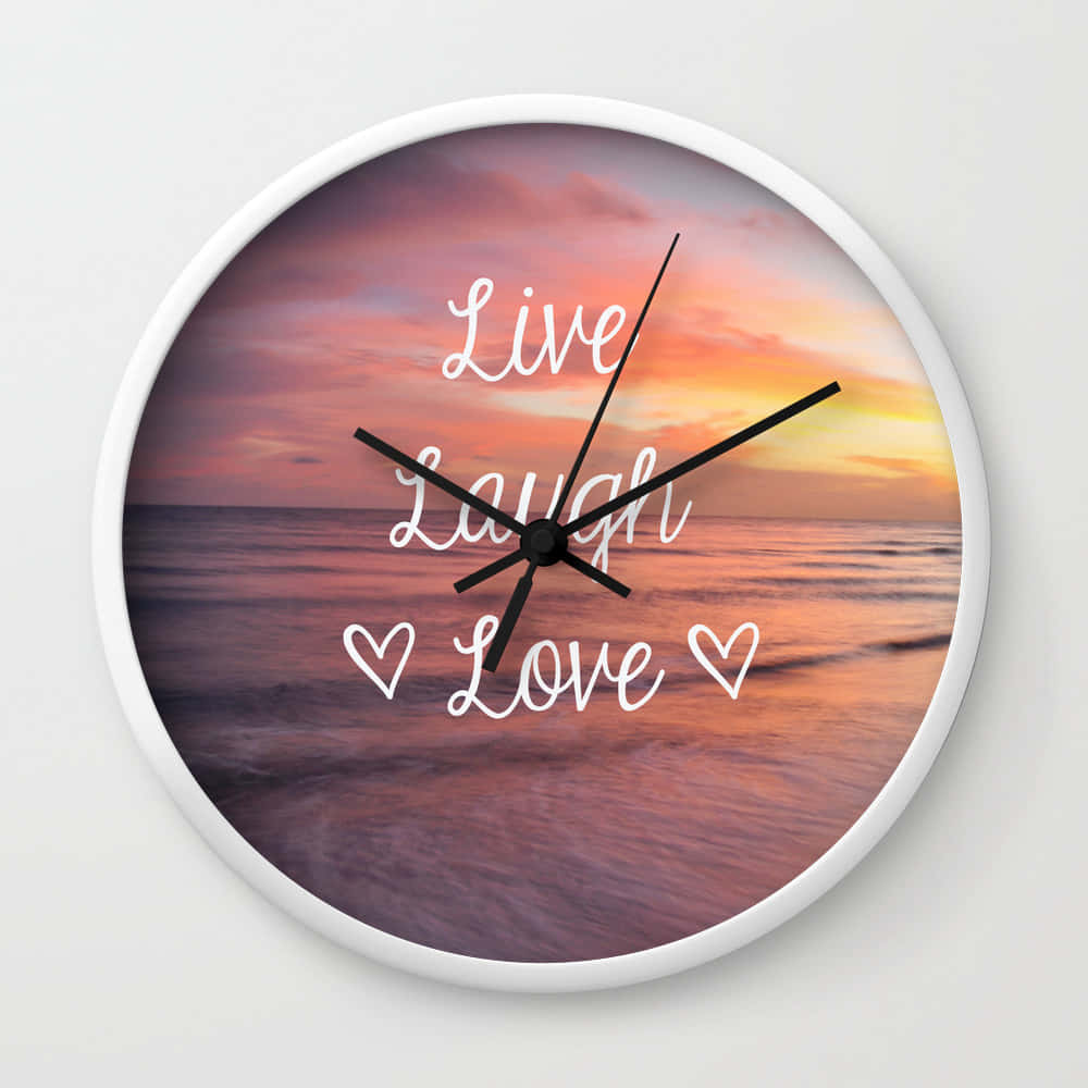 Live Laugh Love 桌布 壁紙 — 一個以海洋日落為背景的掛鐘，以白色草書顯示 Live Laugh Love 字樣並帶有心形符號。
