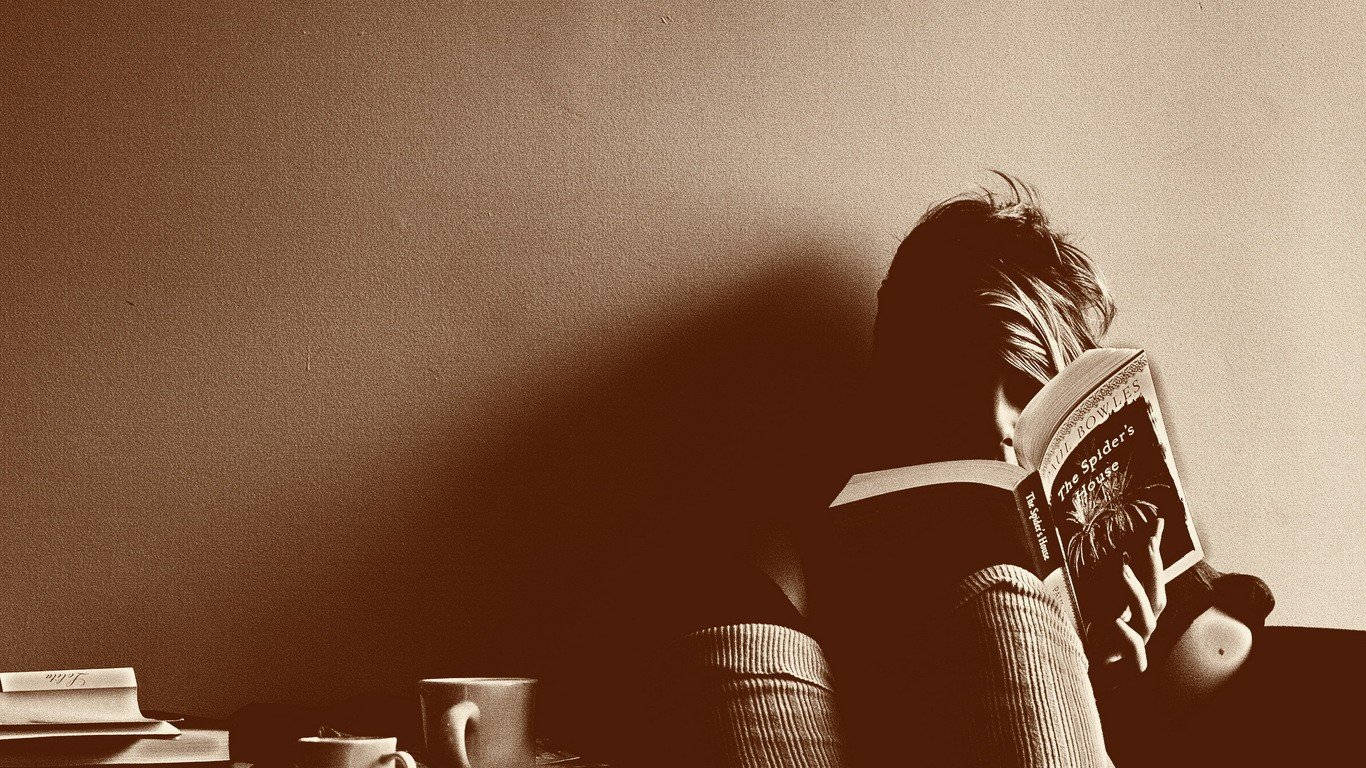 Reading 桌布 壁紙 — 一個以深褐色調呈現的人正在書桌前看書，旁邊有咖啡杯和疊起的書本。