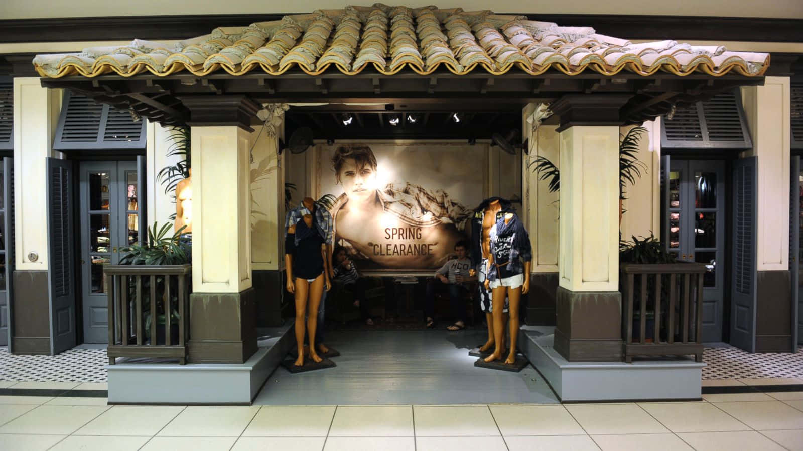 hollister 桌布 壁紙 — 一個以熱帶為主題的零售展示，人體模型在瓷磚屋頂下展示春季清倉服裝。