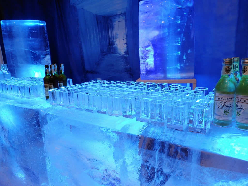 Ice Hotel 桌布 壁紙 — 一個以藍色燈光照亮的冰吧，擺放著一排排水晶酒杯和哈蘭斯海德利口酒瓶。