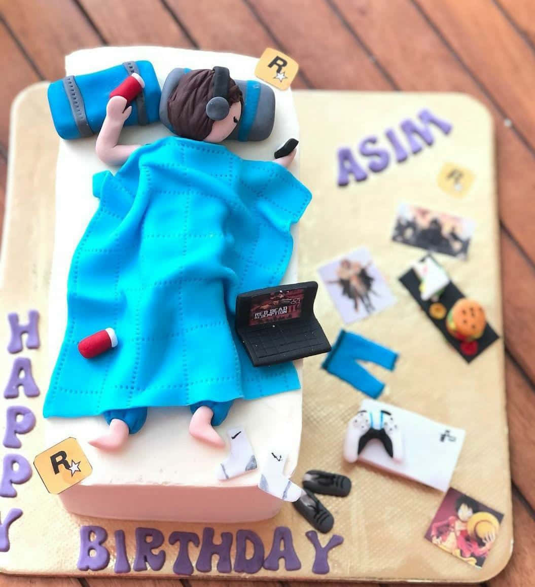 Cake Fondant 桌布 壁紙 — 一個以遊戲玩家為造型的生日蛋糕，躺在床上，周圍有耳機、筆記型電腦、控制器和動漫照片。