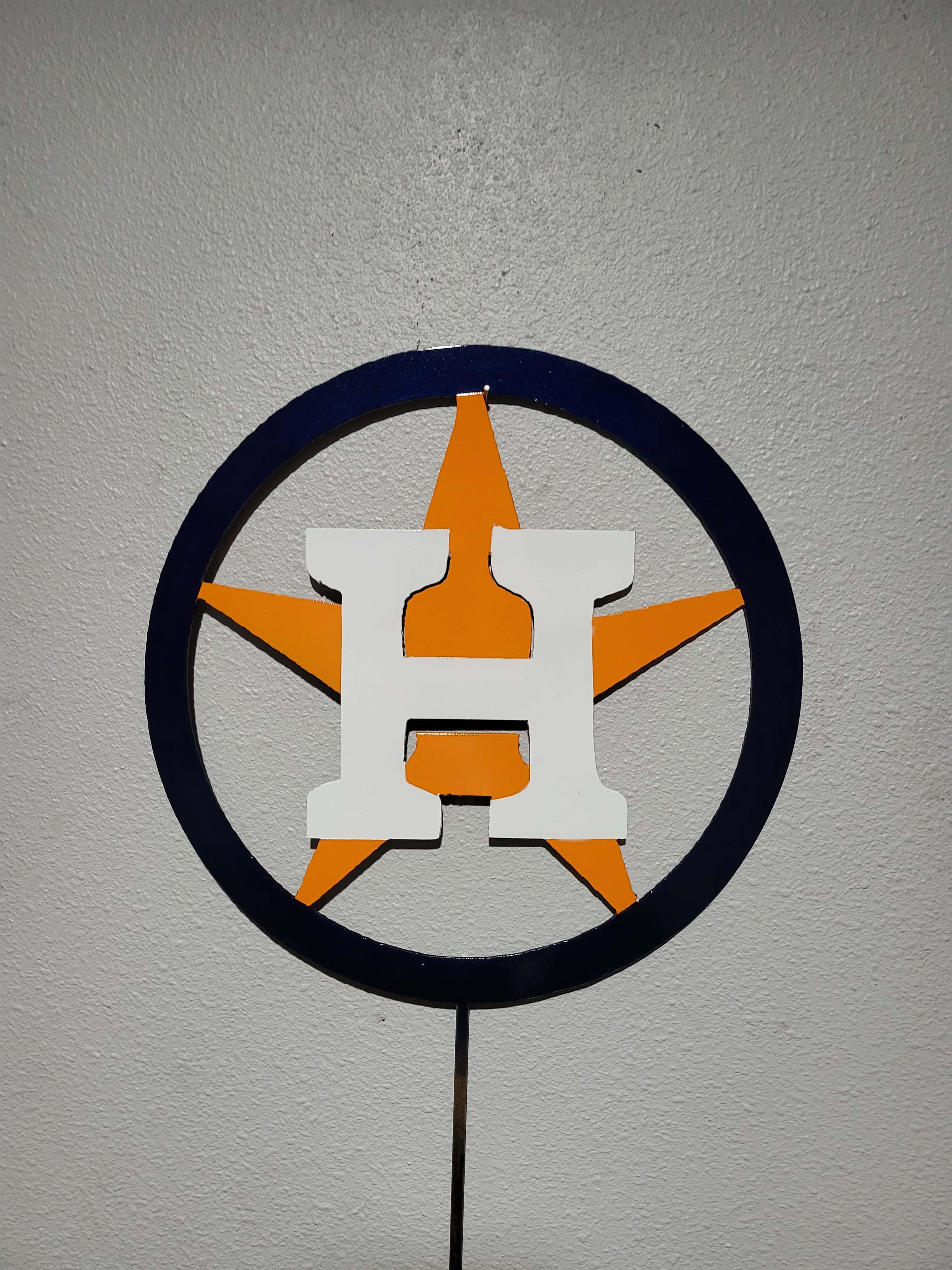 Astros 桌布 壁紙 — 一個休士頓太空人標誌剪影，白色H、橙色星和海軍藍圓圈，安裝在有紋理的牆上。