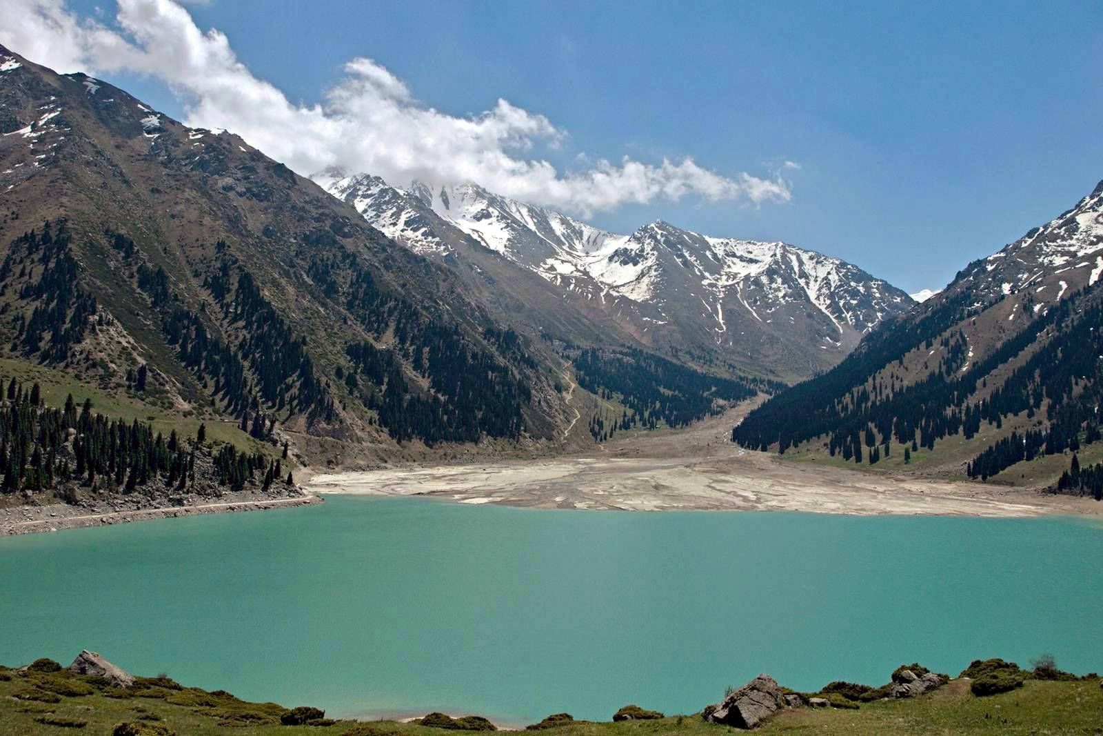 Lake 桌布 壁紙 — 一個位於山谷中的碧綠湖泊，四周環繞著白雪覆蓋的山峰，天空湛藍，雲朵點綴。