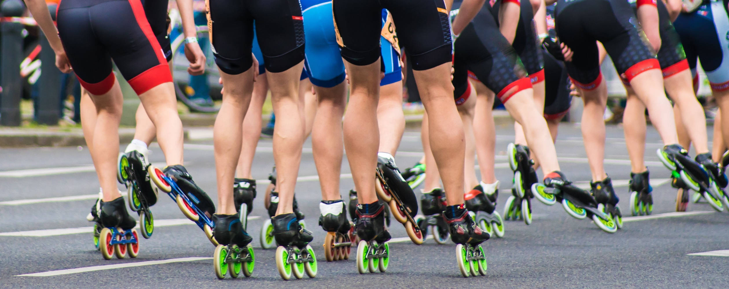 Marathon 桌布 壁紙 — 一個低角度拍攝，穿著色彩繽紛裝備的直排輪滑選手在瀝青賽道上比賽。