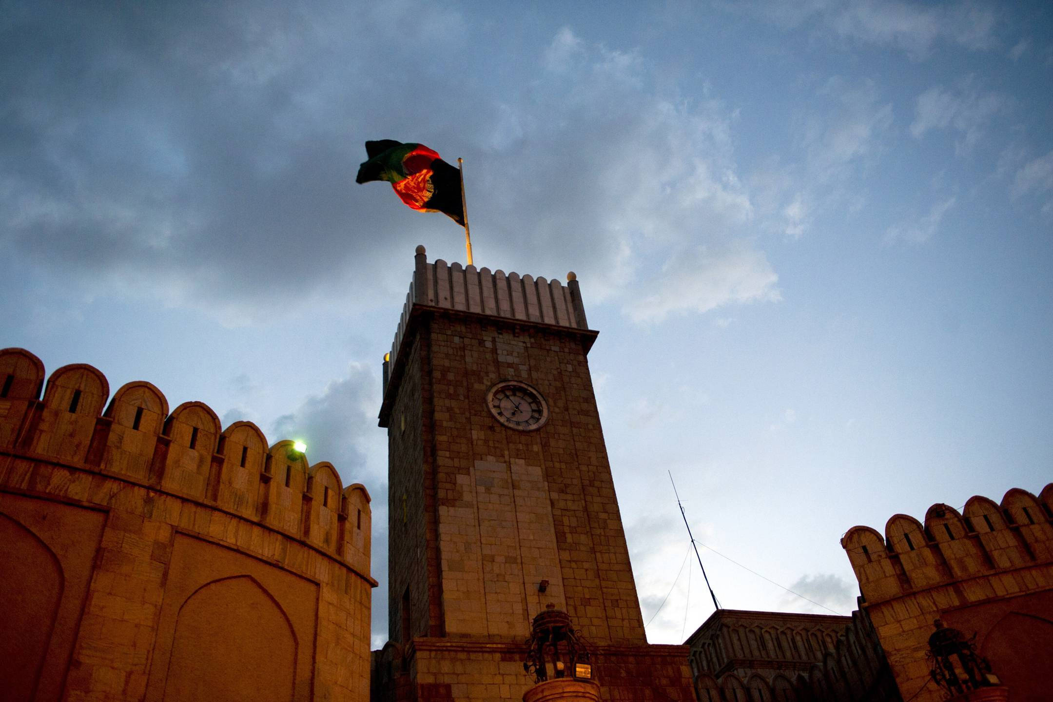 Afghanistan 桌布 壁紙 — 一個低角度拍攝的歷史石造鐘樓，頂上阿富汗國旗在暮色天空中飄揚。