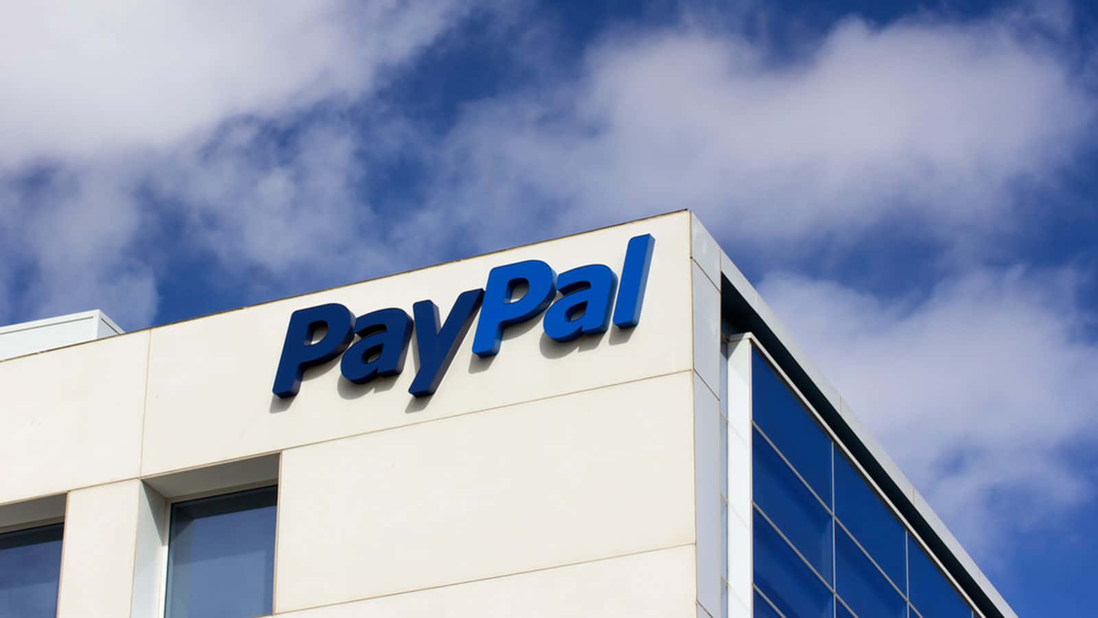 PayPal 桌布 壁紙 — 一個低角度拍攝的現代建築，帶有大型藍色PayPal標誌，背景是明亮的藍天和蓬鬆的白雲。