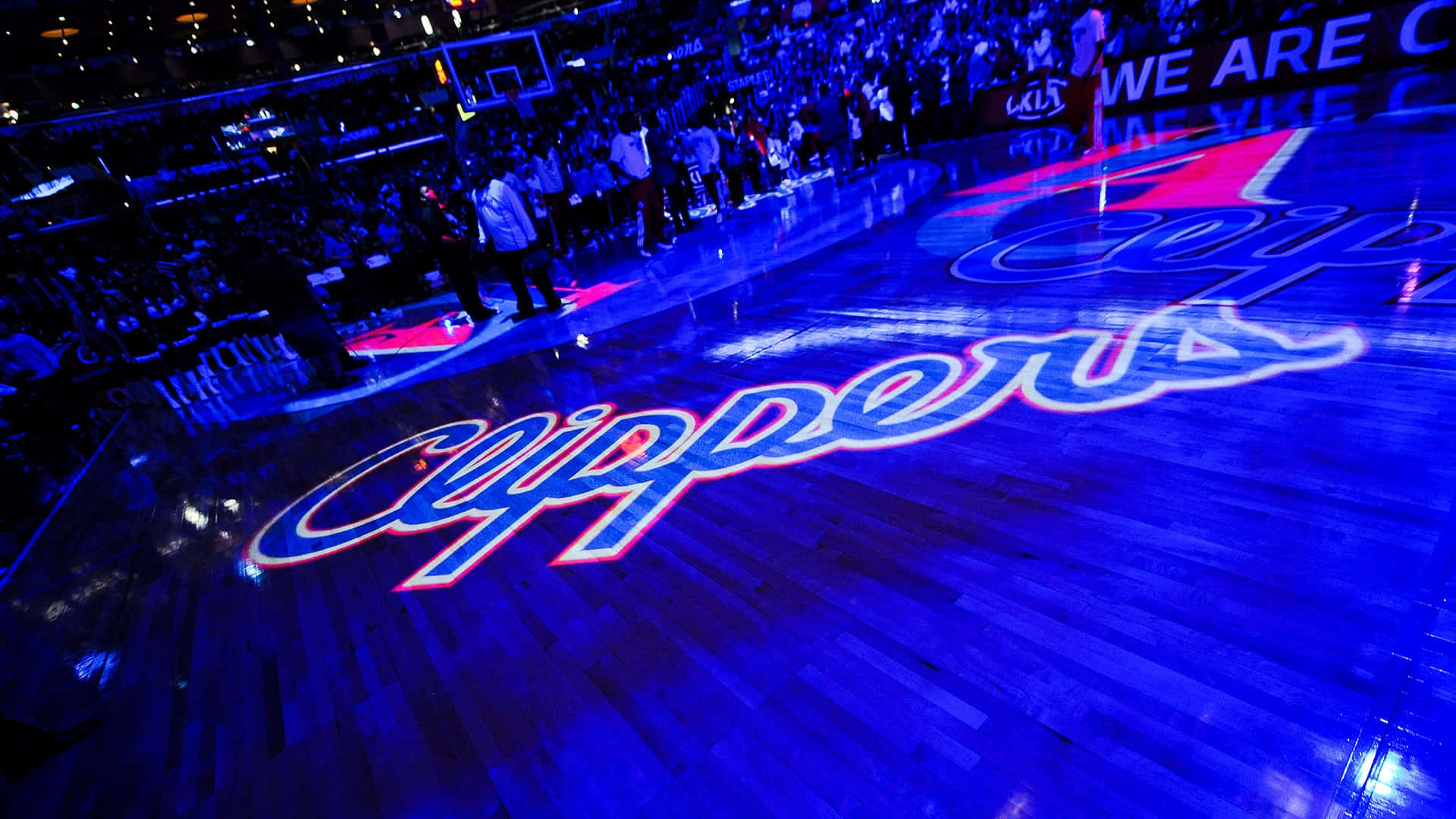 Clippers 桌布 壁紙 — 一個低角度拍攝的籃球場，'Clippers' 標誌在場館燈光下發出藍色和粉紅色的光芒。