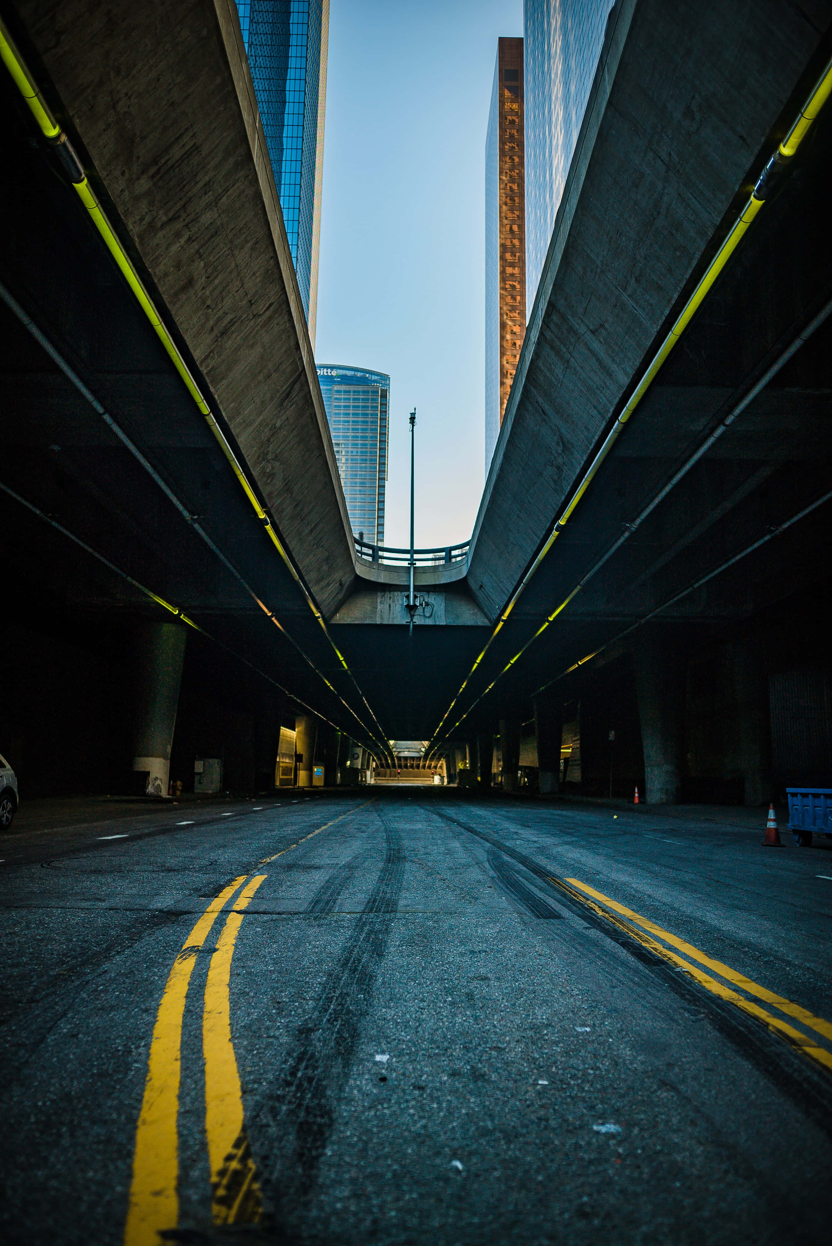 Street 桌布 壁紙 — 一個低角度視角，展示一條空蕩的城市高速公路地下通道，帶有黃色標線和摩天大樓，襯托著暮色天空。