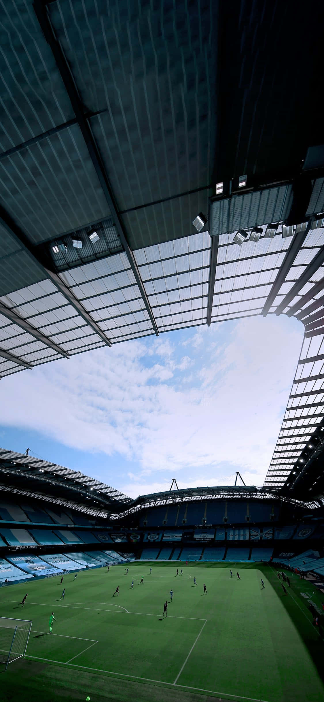 Soccer Stadium 桌布 壁紙 — 一個低角度視角的足球場，場上有球員，天空蔚藍，白雲點綴。
