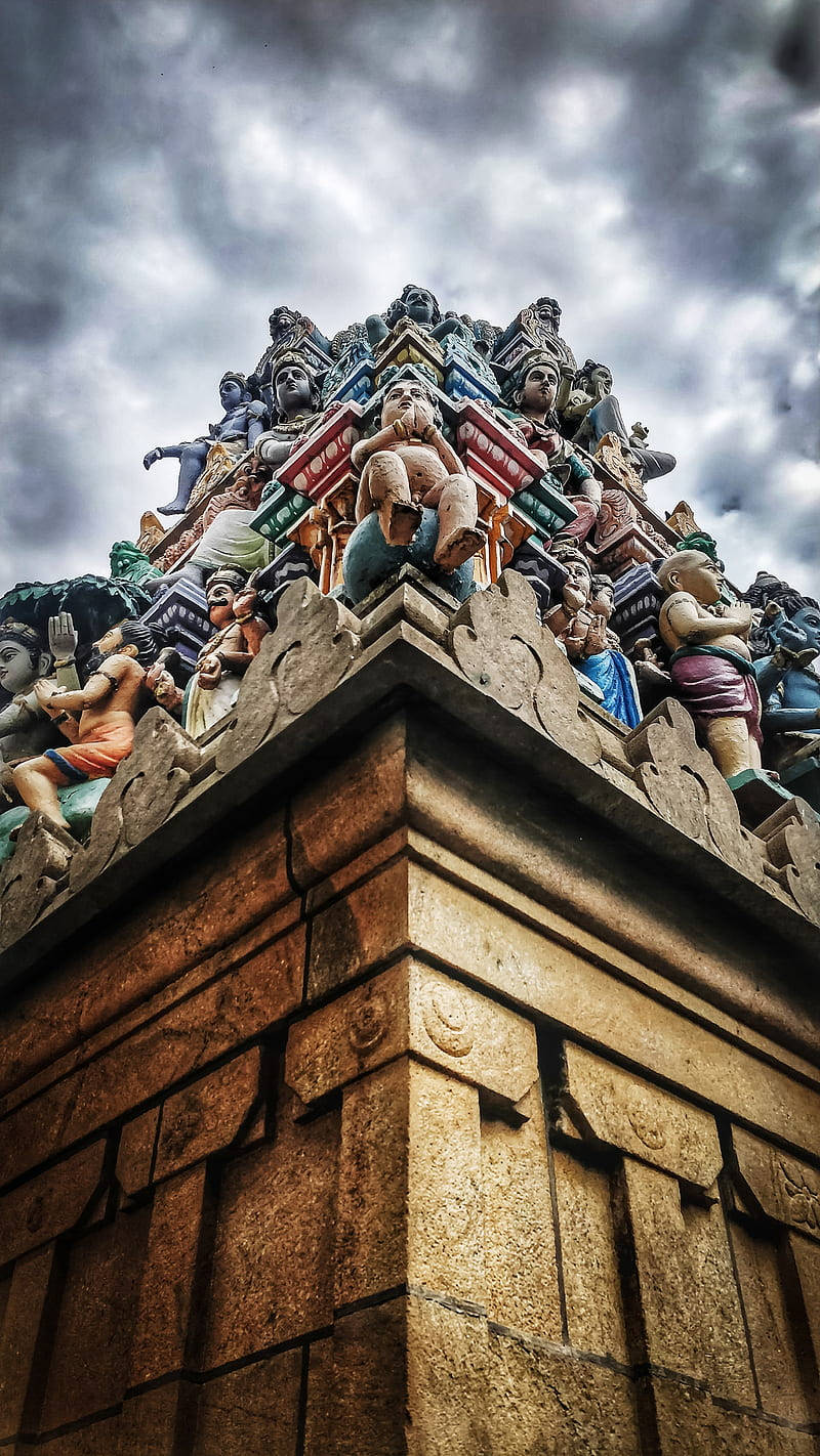 Hindu Temple 桌布 壁紙 — 一個低角度觀看的印度教寺廟門塔，色彩繽紛、雕刻精細，裝飾著色彩繽紛的雕像，背景是戲劇性的多雲天空。