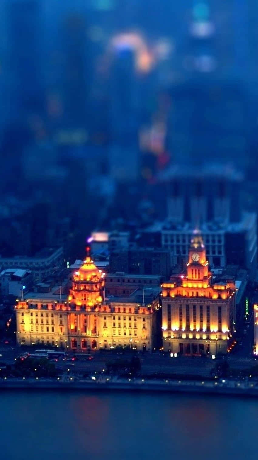 View 桌布 壁紙 — 一個使用移軸效果的夜間城市景觀，溫暖照明的歷史建築在冷藍色模糊背景中閃耀。