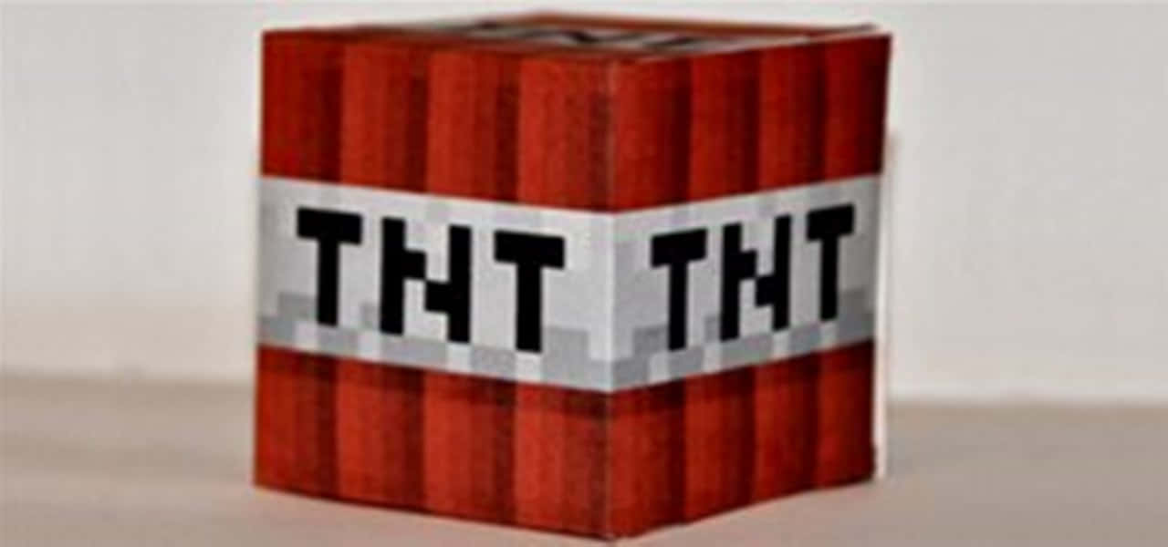我的世界 TNT 桌布 壁紙 — 一個來自Minecraft的像素化紅色TNT方塊放在一個灰色帶上有粗體黑色字體的平坦表面上。