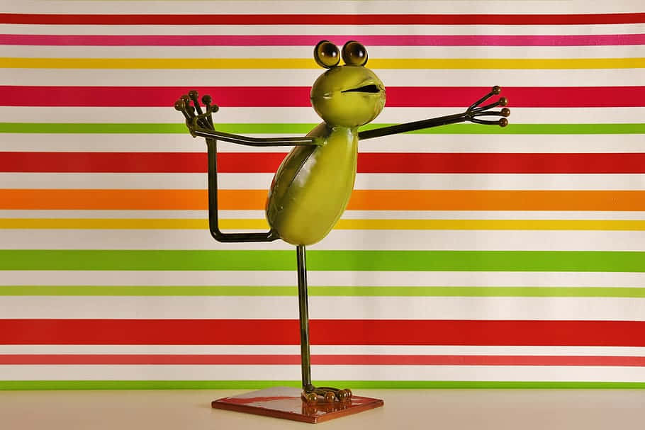 Frog 桌布 壁紙 — 一個俏皮的綠色金屬青蛙雕塑，在充滿活力的條紋背景前擺出瑜珈姿勢。