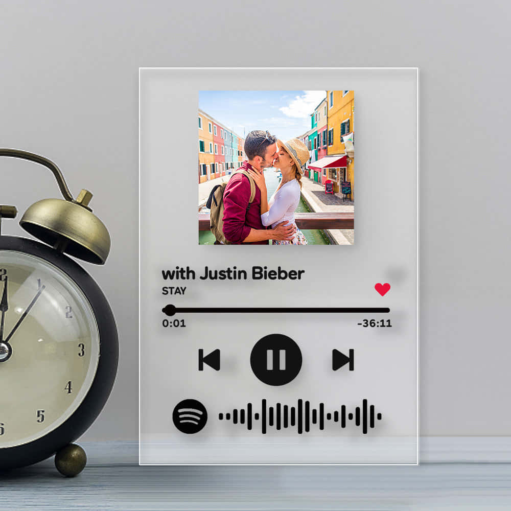 song 桌布 壁紙 — 一個個人化的Spotify音樂播放器框架展示了一對情侶在色彩繽紛的運河邊小鎮接吻，旁邊有一個復古鬧鐘。