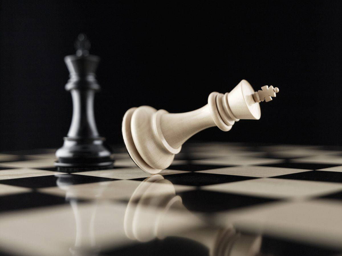 西洋棋 桌布 壁紙 — 一個倒下的白色國王棋在光亮的棋盤上，旁邊站著一個黑色國王棋，在戲劇性的燈光下敗陣。
