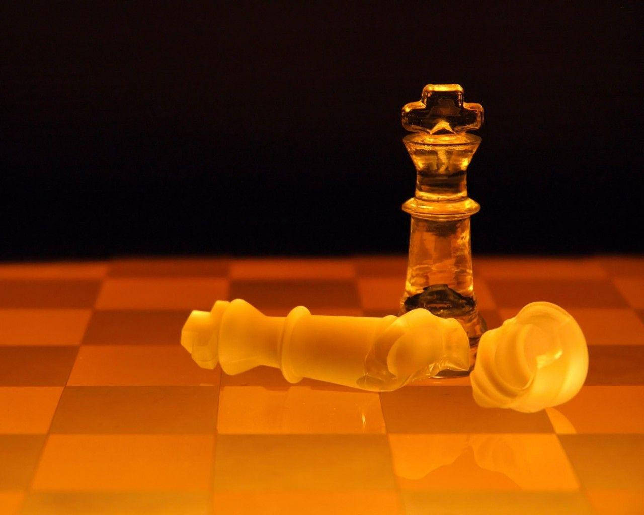 Screen 桌布 壁紙 — 一個倒下的白色西洋棋兵躺在一個站立的琥珀色國王面前，棋盤在溫暖的燈光下，背景黑暗。