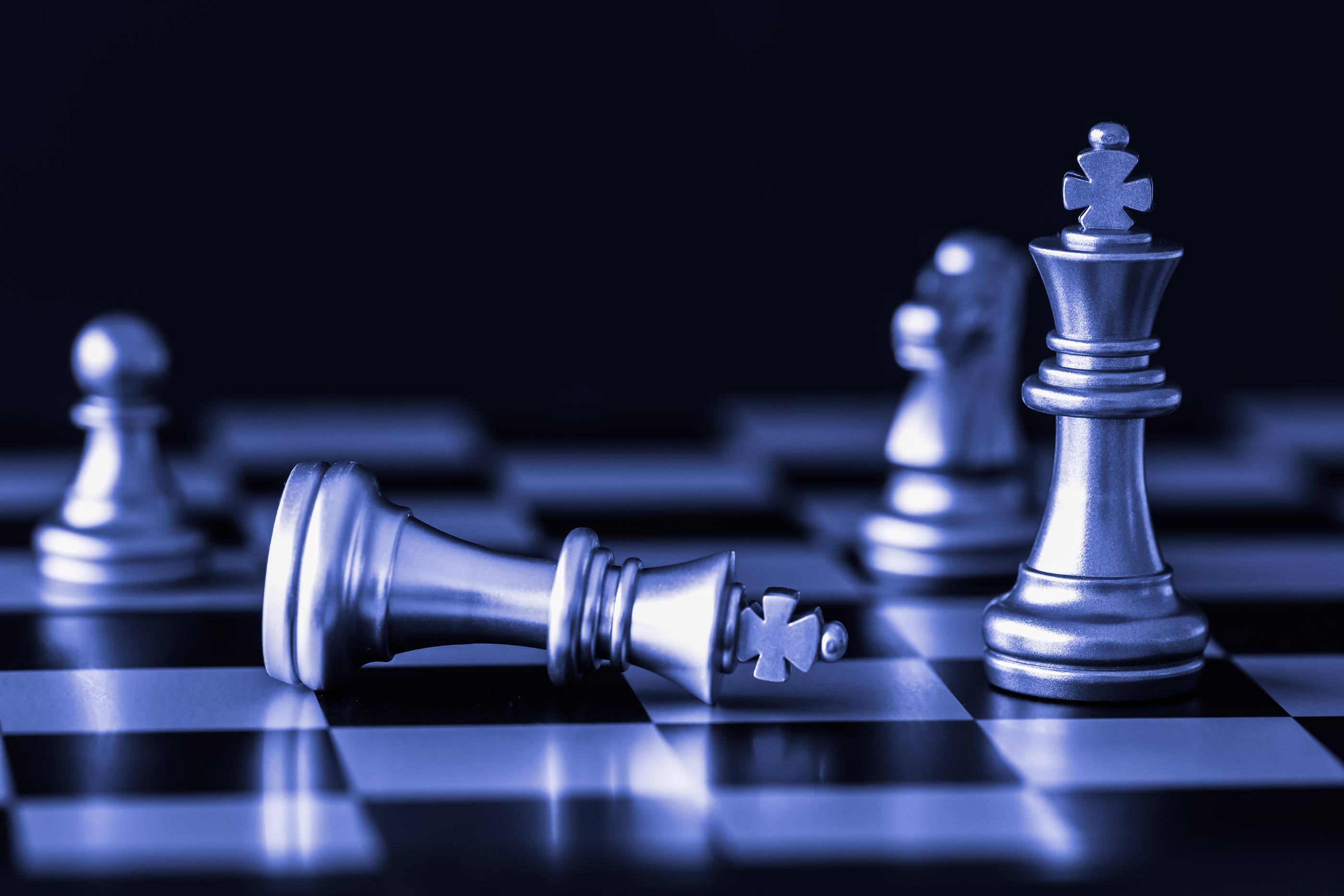 西洋棋 桌布 壁紙 — 一個倒下的銀色西洋棋王躺在棋盤上，旁邊站著一個站立的王，在冷藍色燈光下。