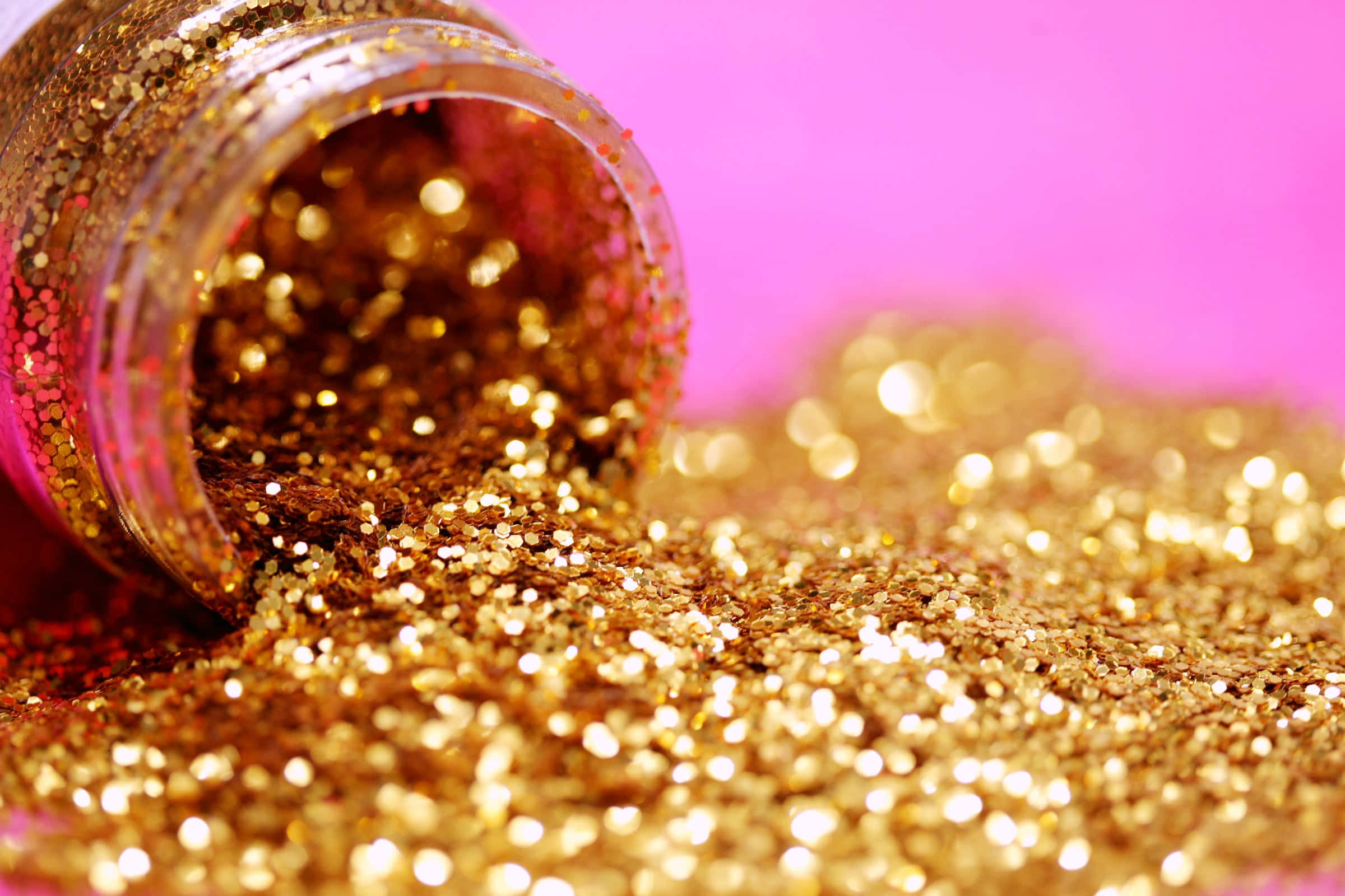 Gold Glitter 桌布 壁紙 — 一個倒出的金色亮粉罐在鮮豔的粉紅色表面上傾瀉而下，形成閃閃發光的紋理前景。