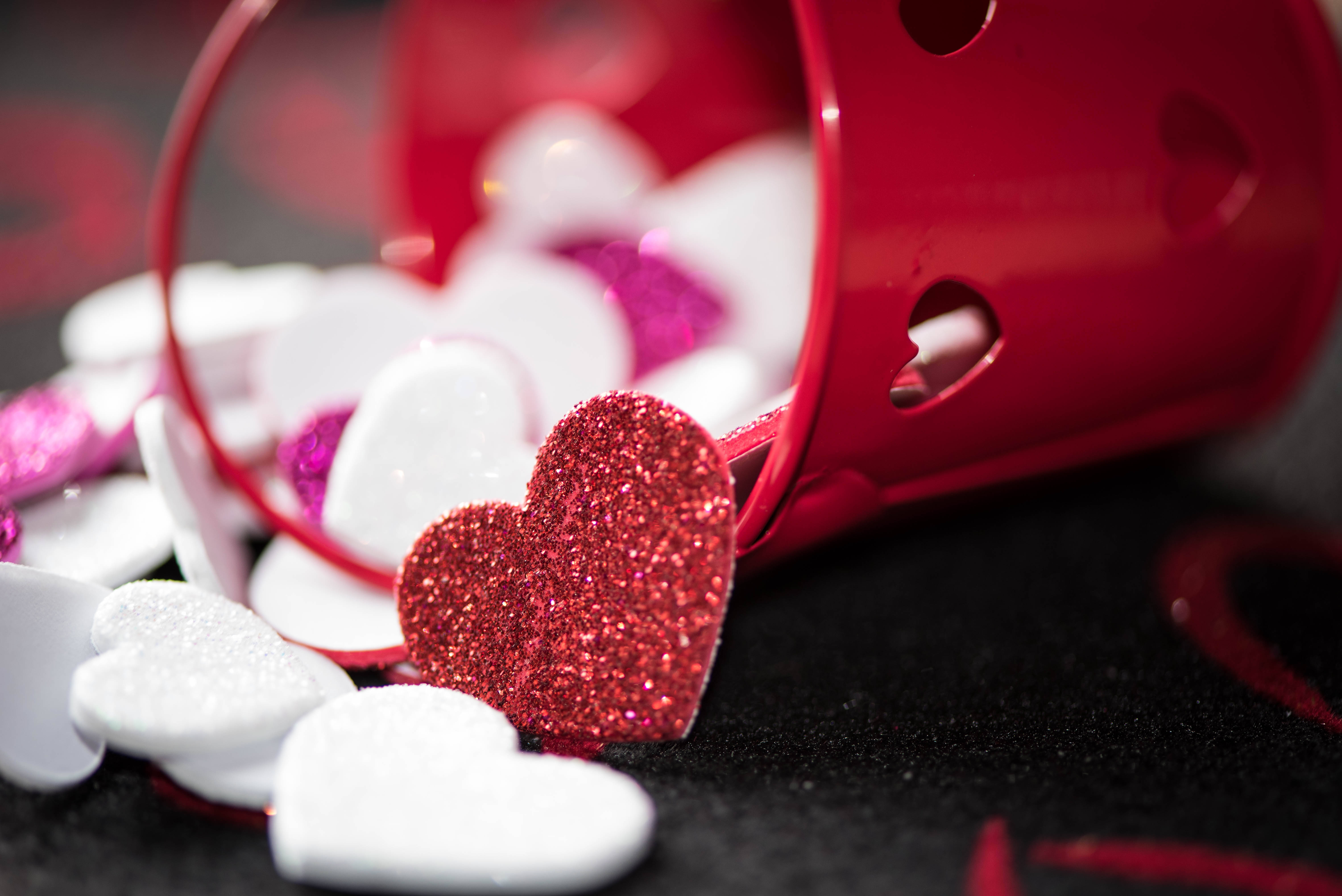 Valentines 桌布 壁紙 — 一個倒翻的紅色杯子在深色紋理表面上溢出閃閃發光的紅色和白色愛心。