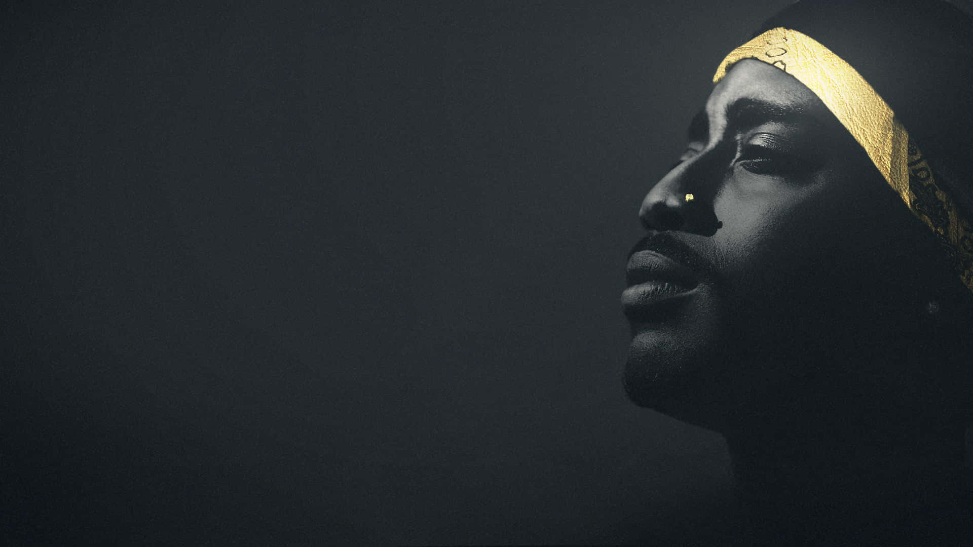 tupac 桌布 壁紙 — 一個側面的男人，戴著金色頭巾，在黑暗的背景中向上凝視。