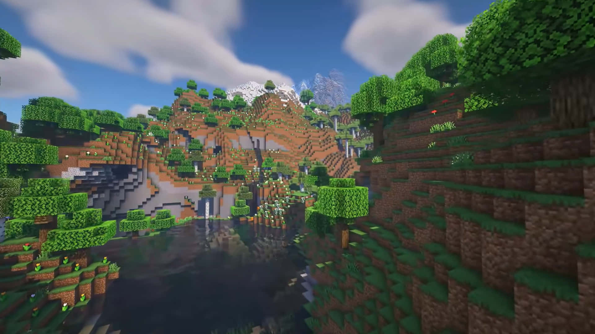 山景 桌布 壁紙 — 一個像素化的Minecraft景觀，有茂密的綠色樹木、棕色山丘和一道瀑布流入平靜的湖泊，上方是明亮的藍天和蓬鬆的雲朵。