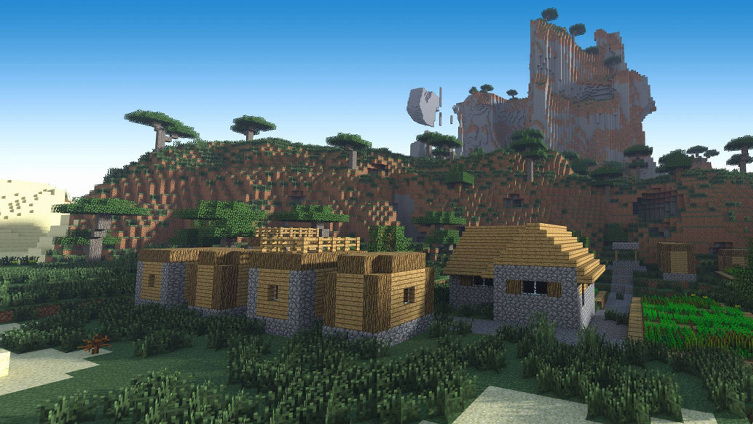 我的世界 高畫質壁紙 桌布 壁紙 — 一個像素化的Minecraft村莊，坐落在長滿草的谷地中，有木屋、石頭地基和背後高聳的懸崖。
