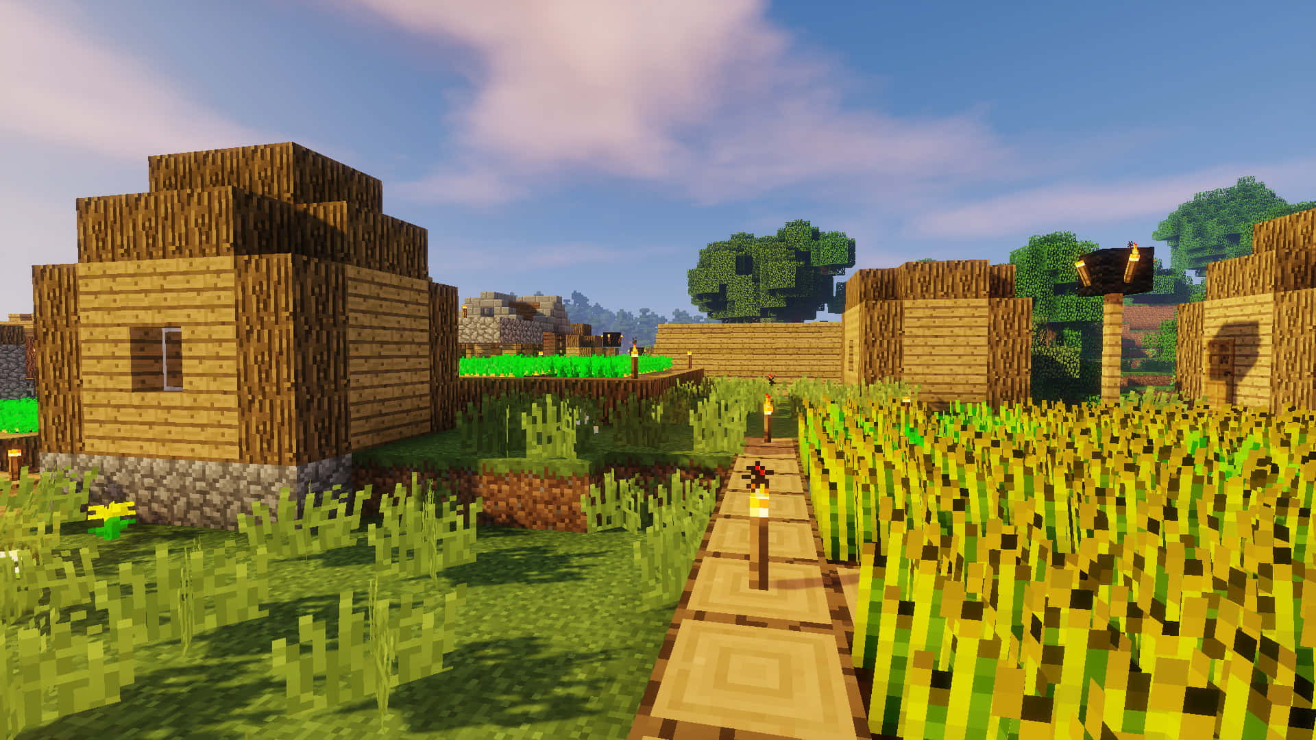 Minecraft Villages 桌布 壁紙 — 一個像素化的Minecraft村莊，有木屋和火炬照亮的小路，周圍環繞著高大的草和樹木，在明亮的藍天下。
